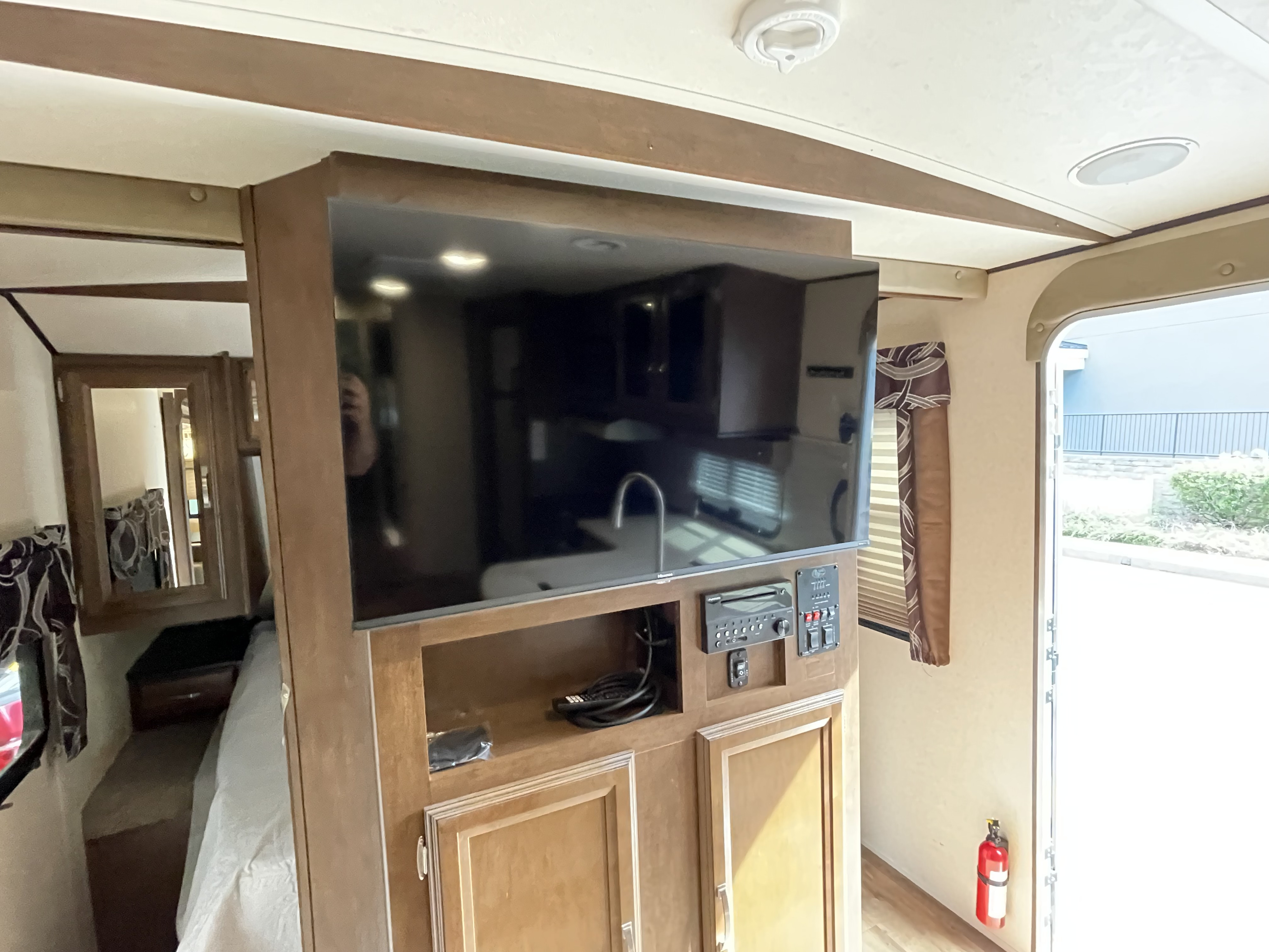 Inside an RV rental: living area with TV, entertainment system, and kitchen reflection. Bedroom and exit door visible.. Forest River Wildwood Heritage Glen Lite 2018
