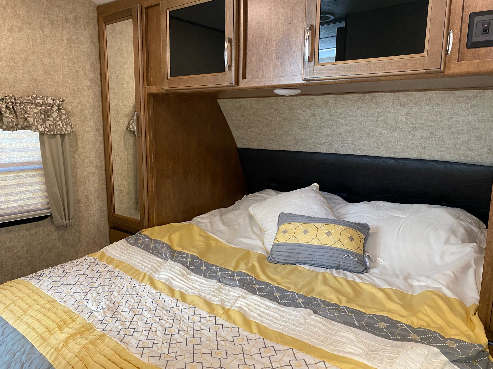 Cozy RV rental bedroom with warm yellow and grey bedding, overhead cabinets, and window for a comfortable stay.. Forest River Wildcat 2018