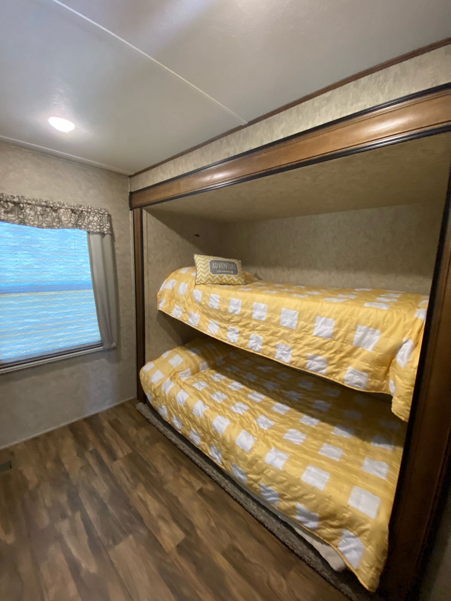 Inside an RV rental: two comfy bunk beds with bright yellow and white checkered bedding. Features a window, wood floor, and overhead light.. Forest River Wildcat 2018
