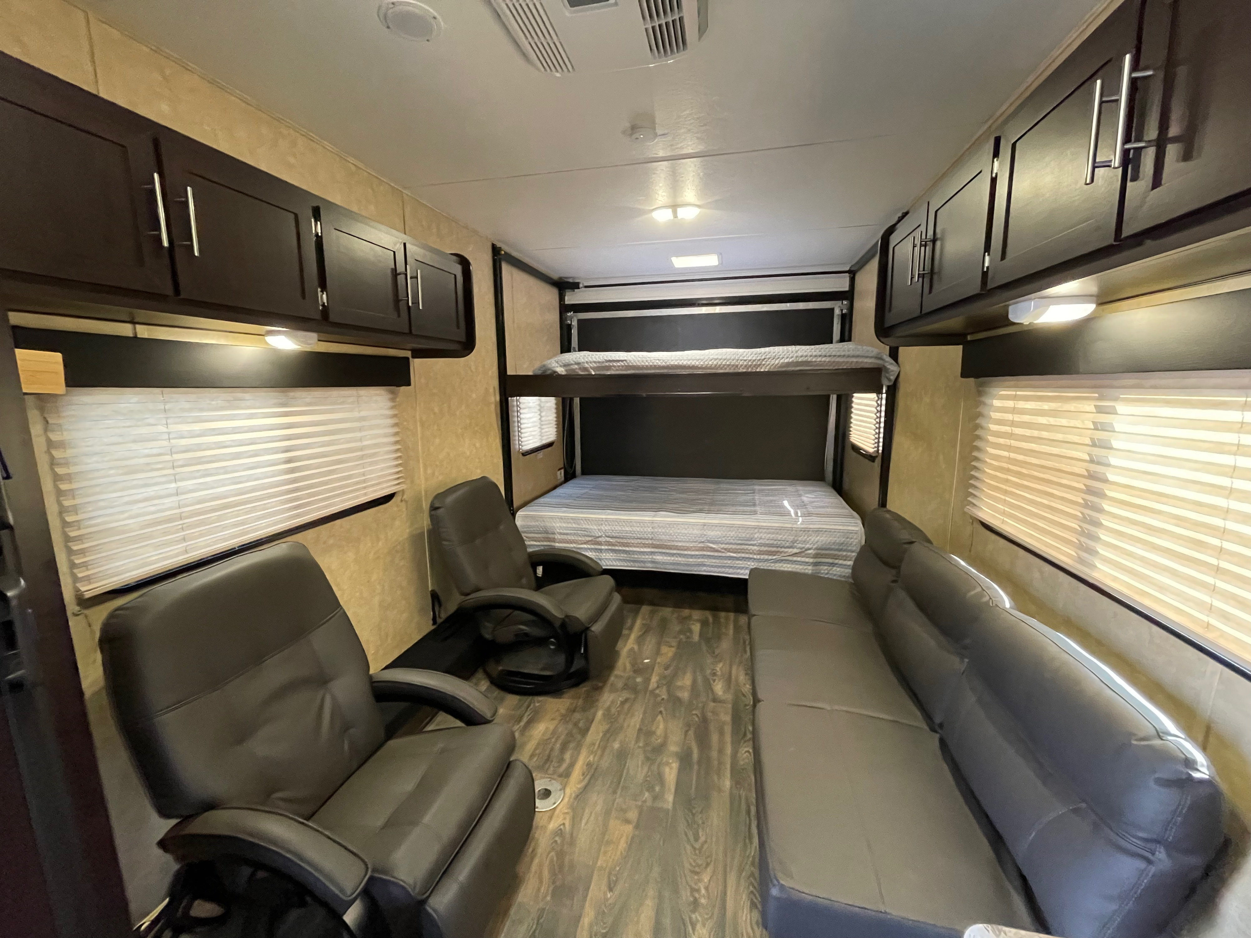 Spacious rv rental interior with a bunk bed, two recliners, and a sofa, featuring overhead cabinets and wood-look flooring.. Dune Sport Toy Hauler 2017
