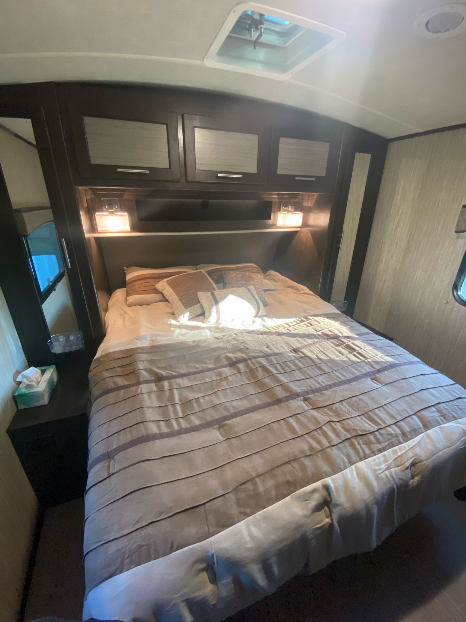 Cozy RV rental bedroom with a striped comforter, overhead storage cabinets, and warm bedside lighting. Perfect for your next adventure.. Cruiser Rv Corp Fun Finder 2018