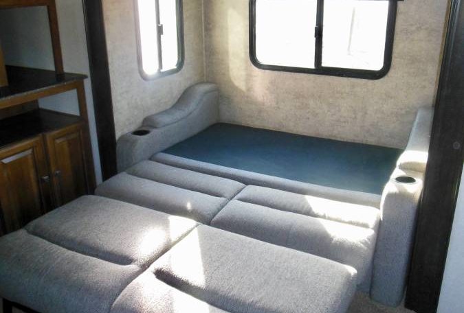 RV rental interior: Gray fabric sofa bed extended for sleeping, featuring cupholders, windows, and cabinetry.. Coachmen Freedom Express 2017