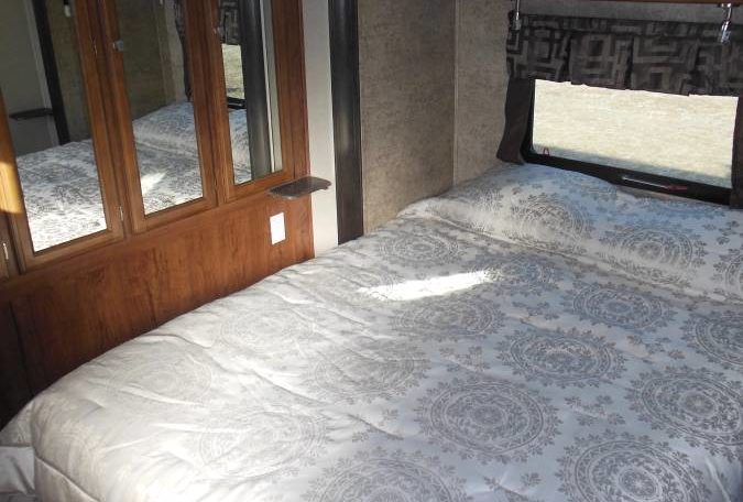 RV rental bedroom featuring a comfy bed with patterned bedding, window, and mirrored storage.. Coachmen Freedom Express 2017