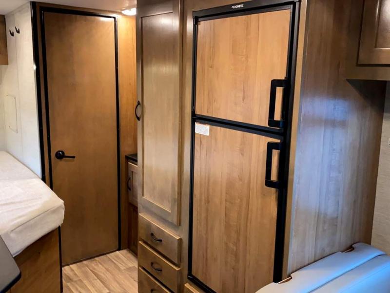RV rental interior showing a compact camper living space with a bed, Dometic refrigerator, and wooden cabinetry.. Tiffin Motorhomes Wayfarer 2021