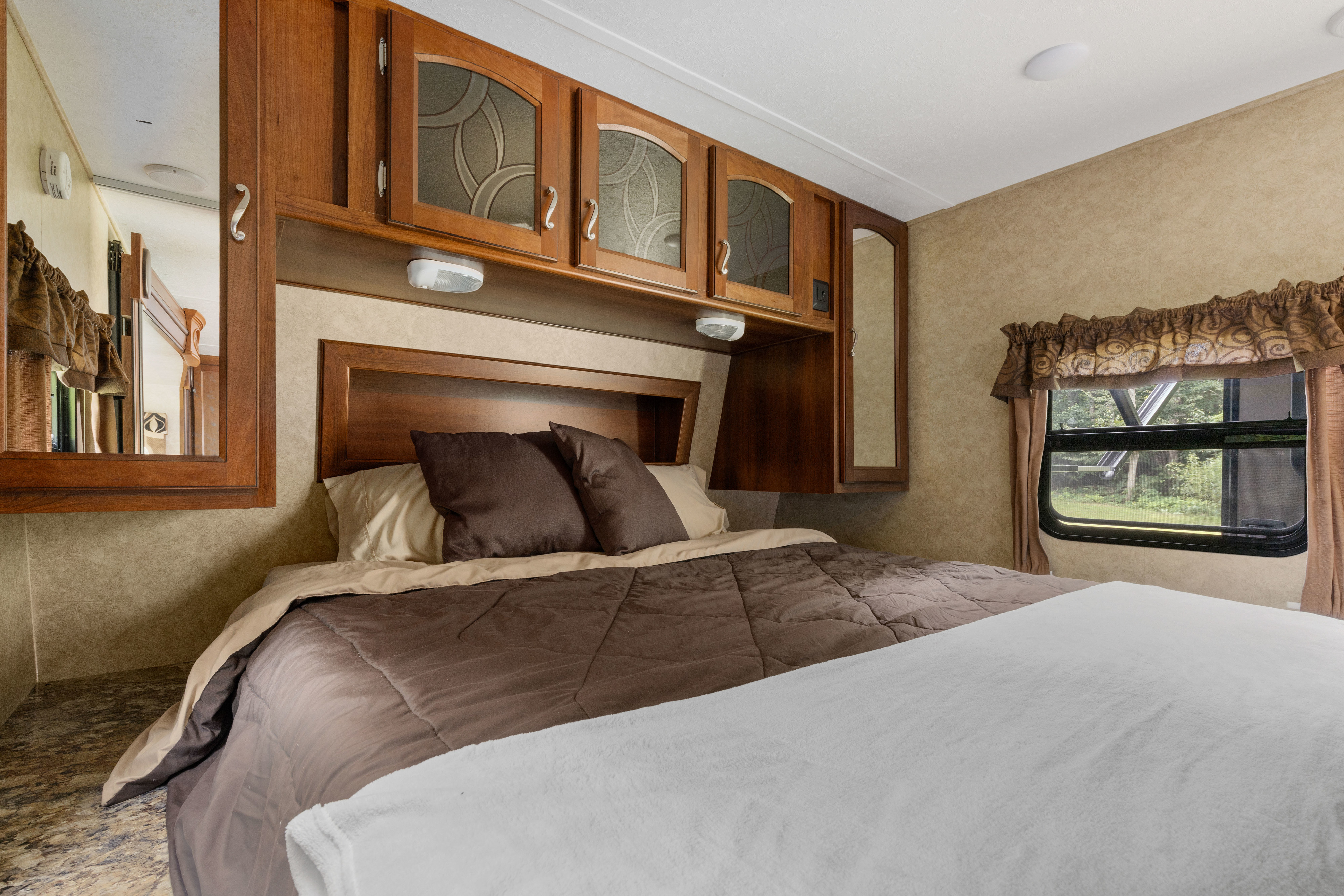 Inviting RV rental bedroom: brown comforter, ample wooden cabinets, and a window to nature. Ideal for comfortable travel.. Prime Time Tracer 2014