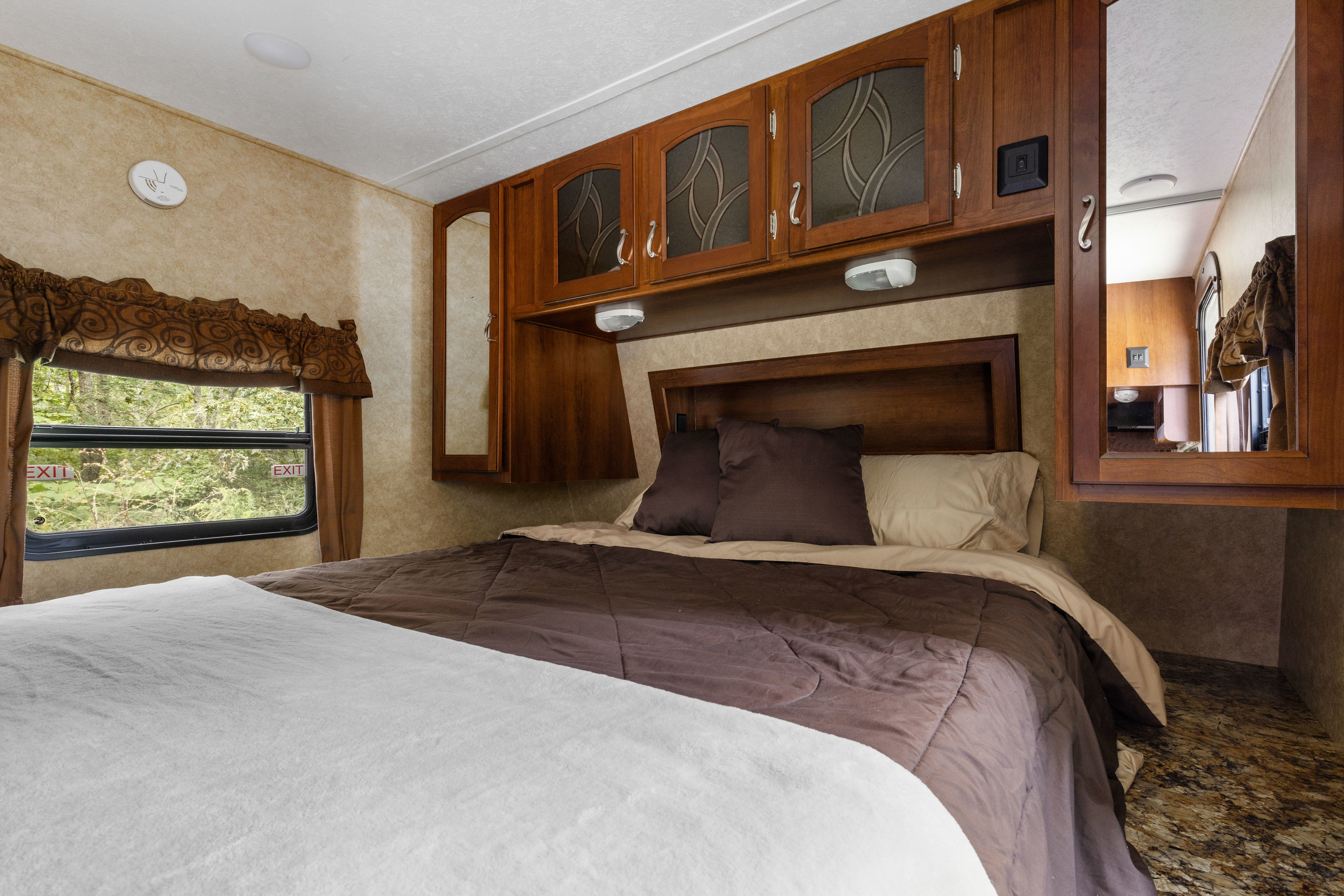 Interior of an RV rental bedroom featuring a cozy bed, ample overhead storage, and a window displaying a lush outdoor view.. Prime Time Tracer 2014