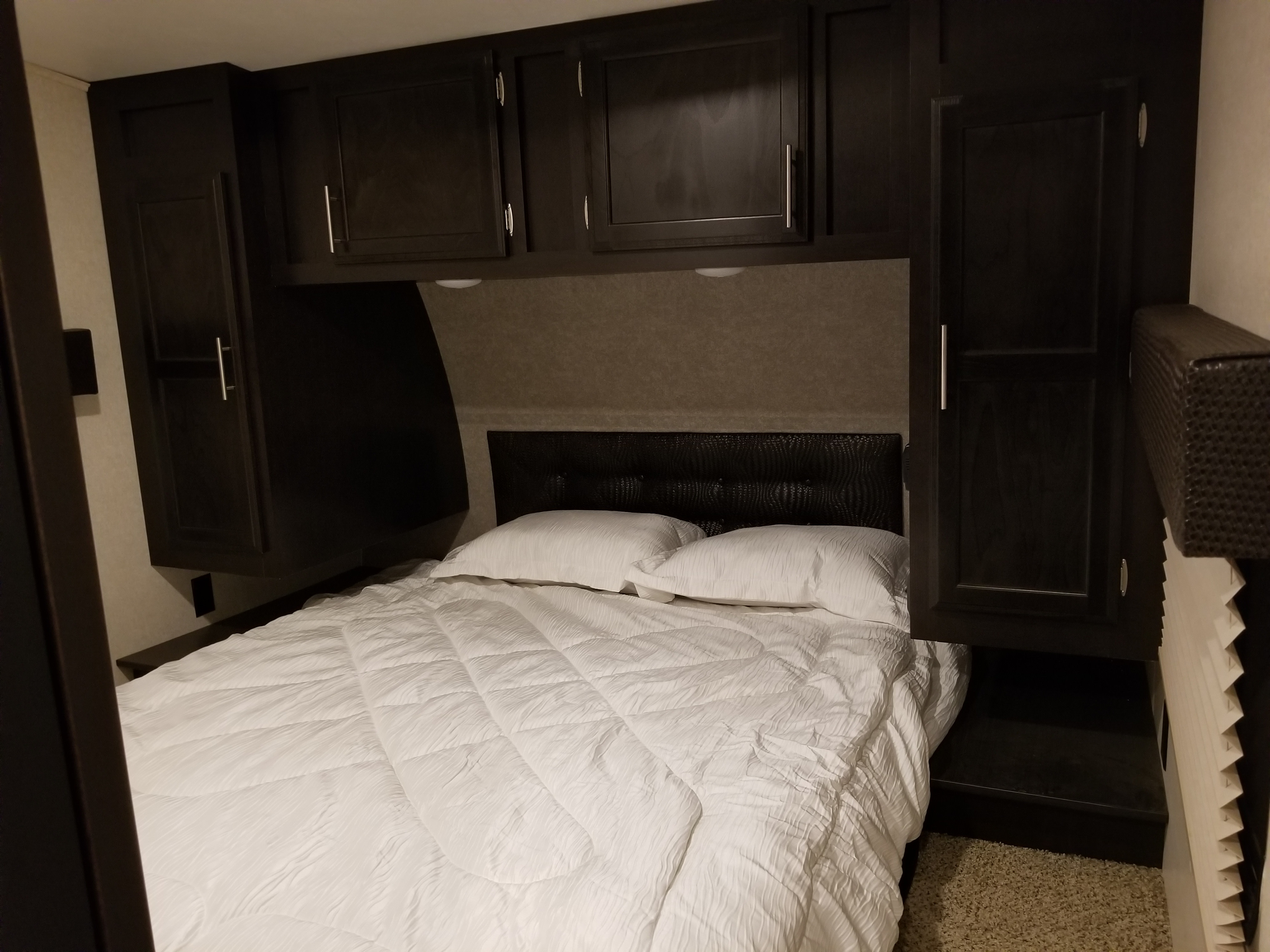 RV rental bedroom: cozy space with white bed, dark cabinets, and a textured black headboard.. Jayco Octane 2017
