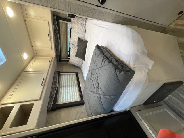 Clean and modern RV rental bedroom featuring a comfortable bed, overhead cabinets, and windows with blinds.. Thor Motor Coach Four Winds 2022