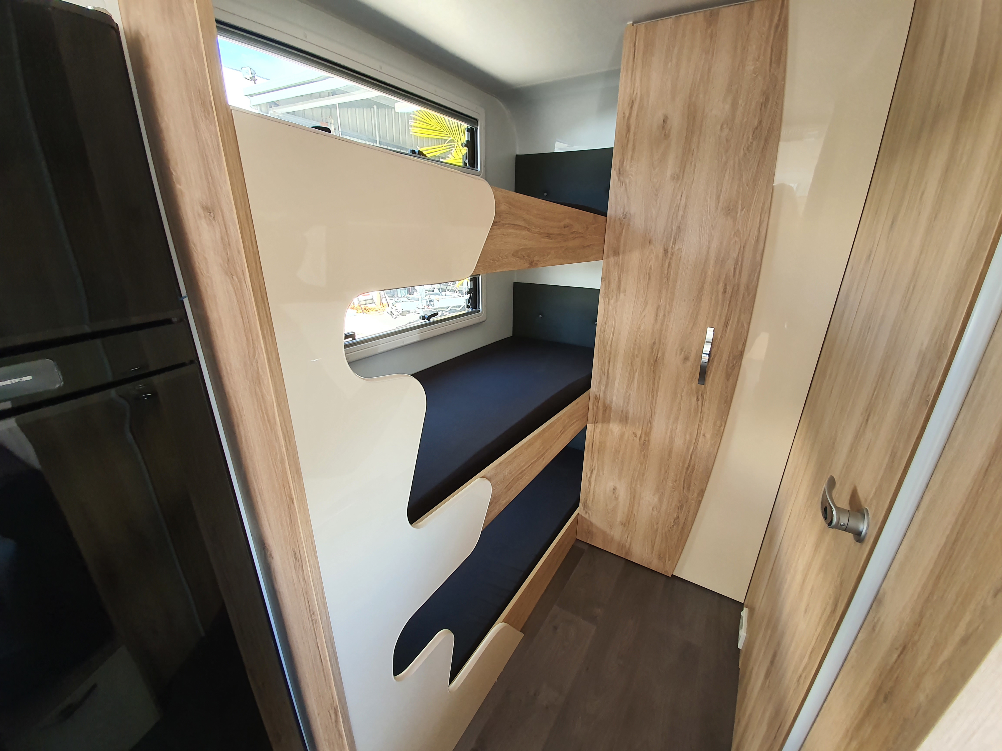Inside an RV rental: modern bunk beds with cream accents, built-in fridge, and wood wardrobe maximize space.. Avan Aspire 617 Family 2021