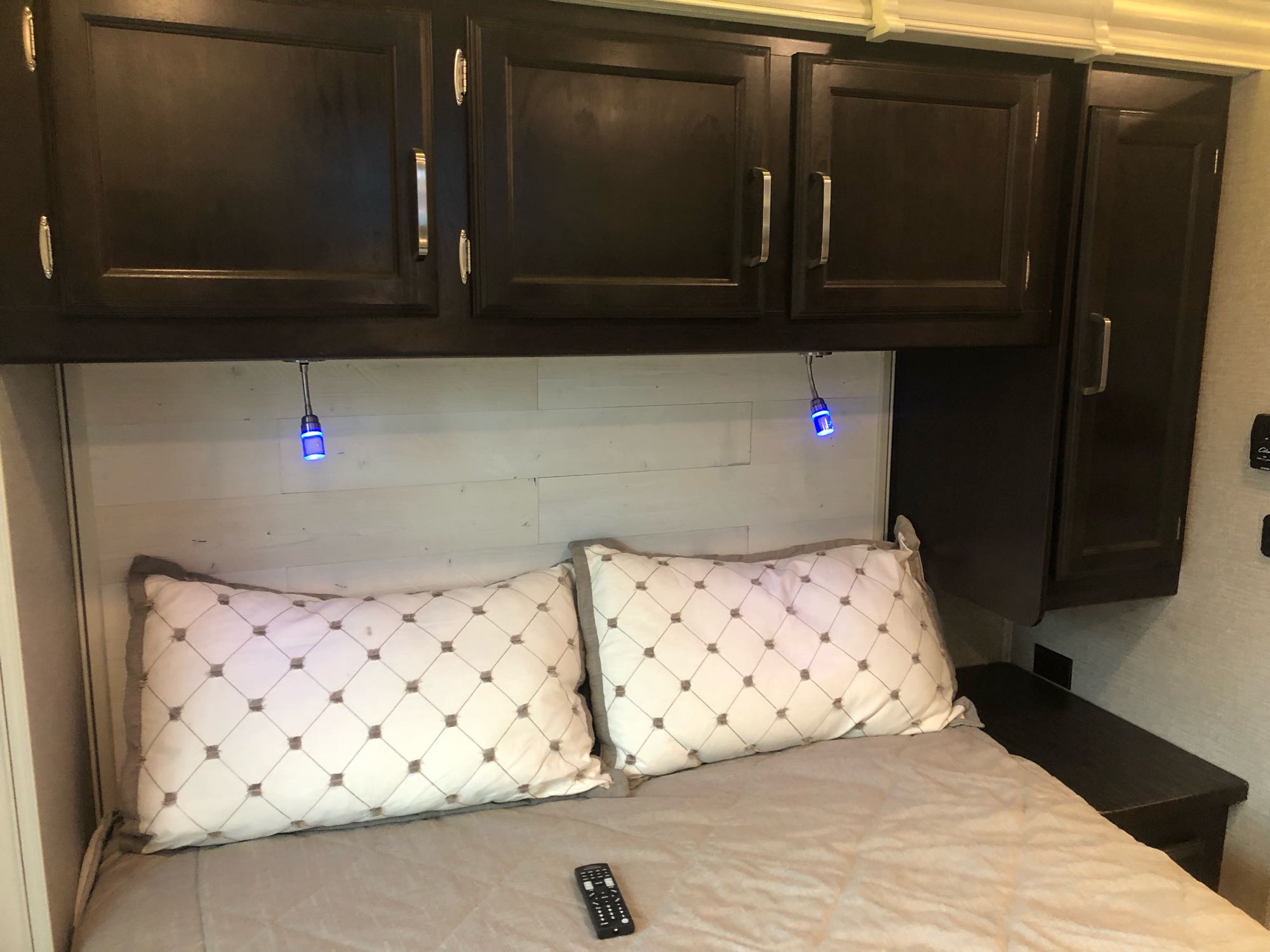 Well-appointed RV rental bedroom with dark wood cabinets, blue reading lights, and patterned pillows on a comfortable bed.. Jayco Greyhawk 2021