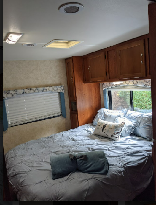 Comfortable RV rental bedroom with blue bedding, window, and wood cabinets. Ideal for travel.. Forest River Coachmen Freelander 2011
