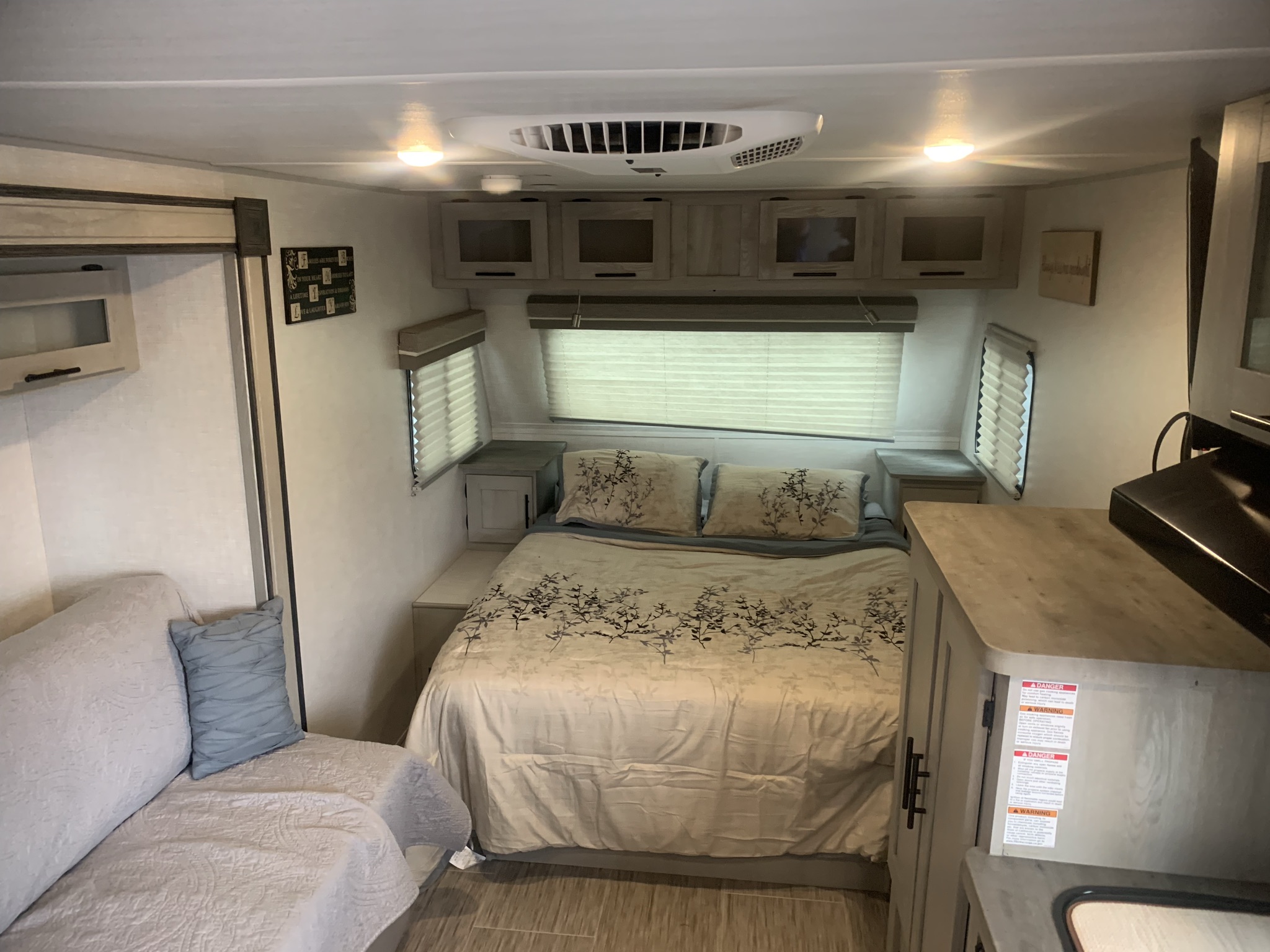 This rv rental interior features a cozy bedroom area with a full bed, sofa, compact kitchen, and ample overhead storage.. Forest River Ibex 2021