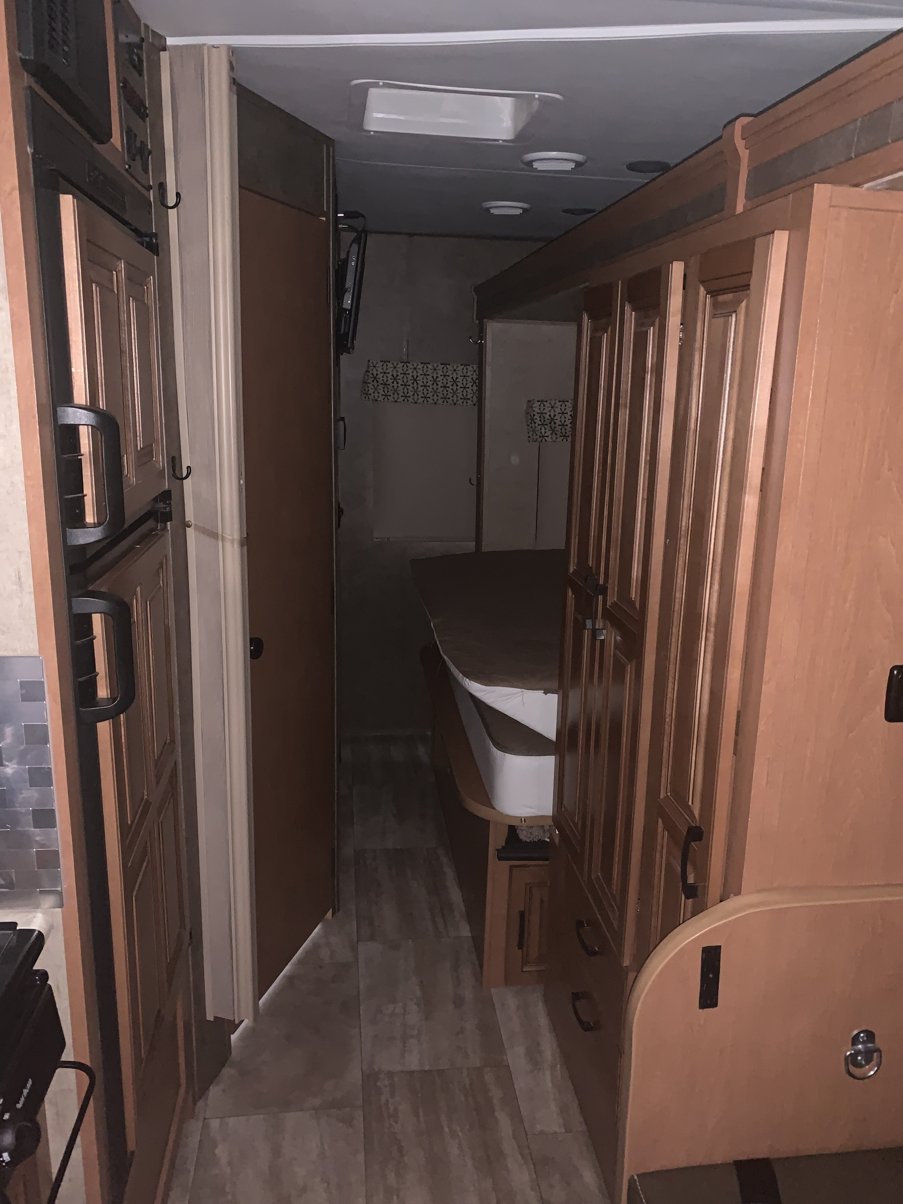 Spacious RV rental interior: Central hallway with kitchen cabinetry on left, leading to a bedroom with a bed and wardrobe.. Forest River Sunseeker 2017