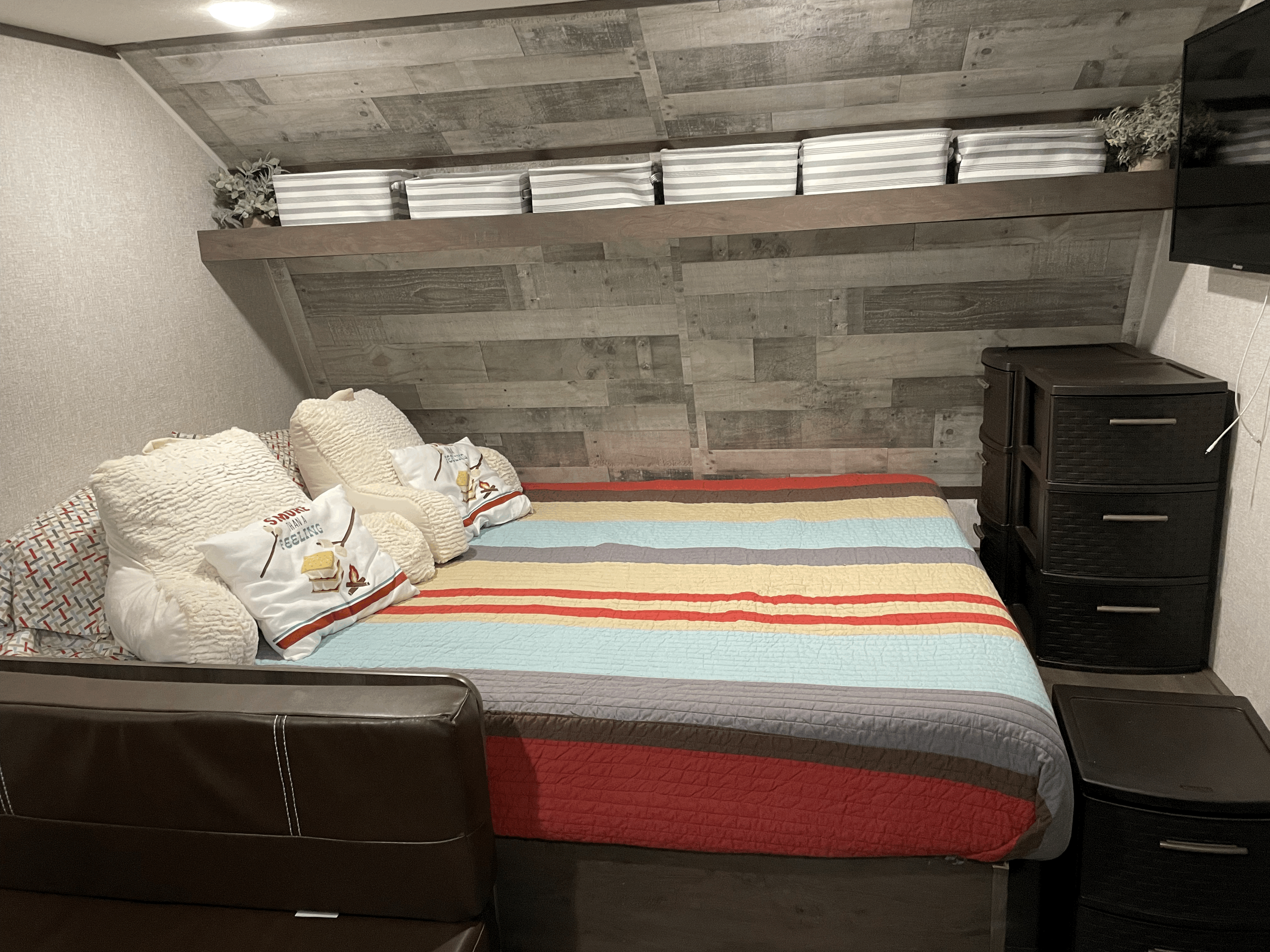 RV rental bedroom with a colorful striped bed, plush pillows, overhead storage bins, and plastic drawers.. Coleman Other 2022
