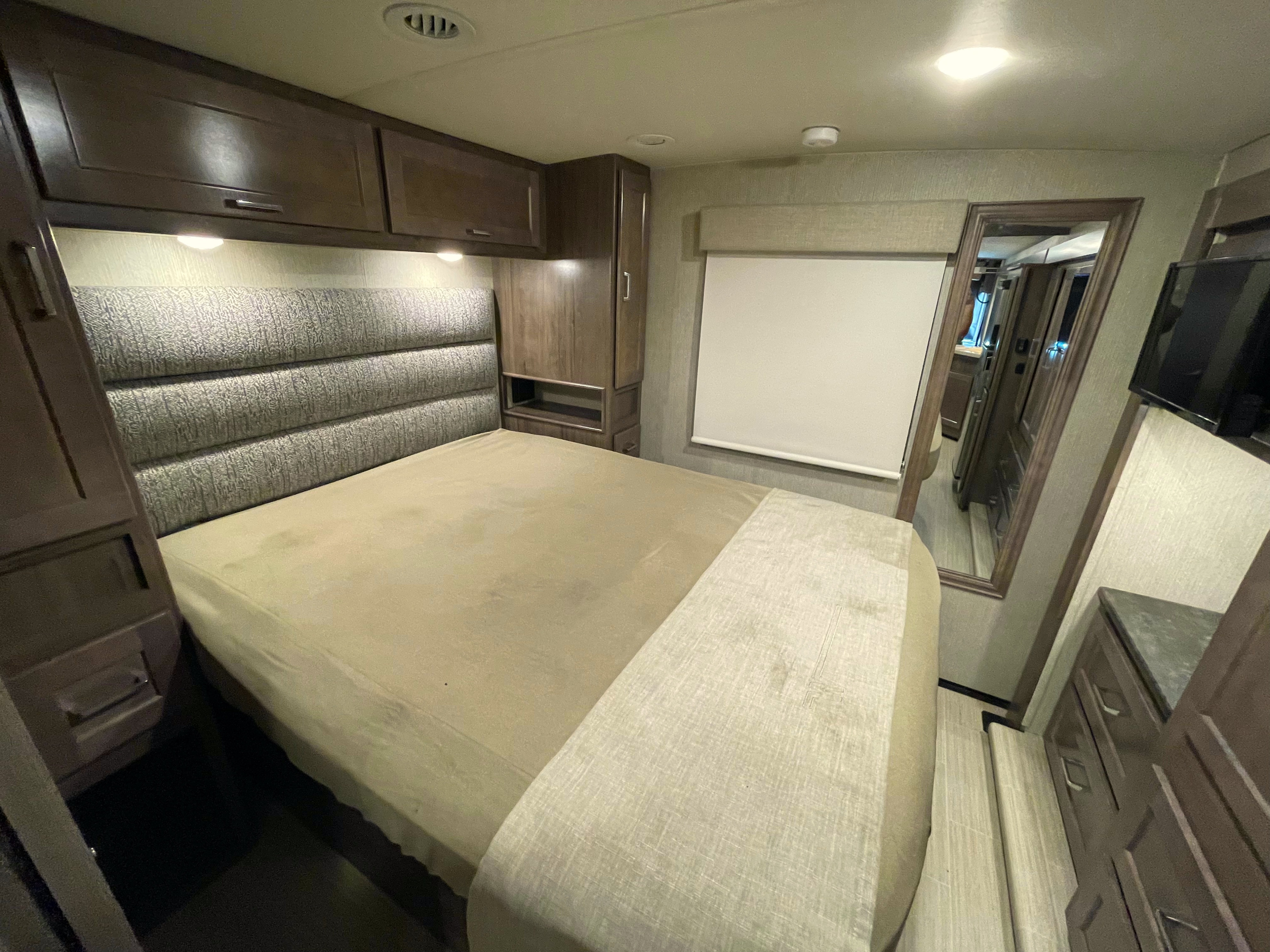 Interior of an RV rental bedroom, showcasing a comfortable bed, wood cabinets, a full-length mirror, and TV.. Winnebago Adventurer 2022