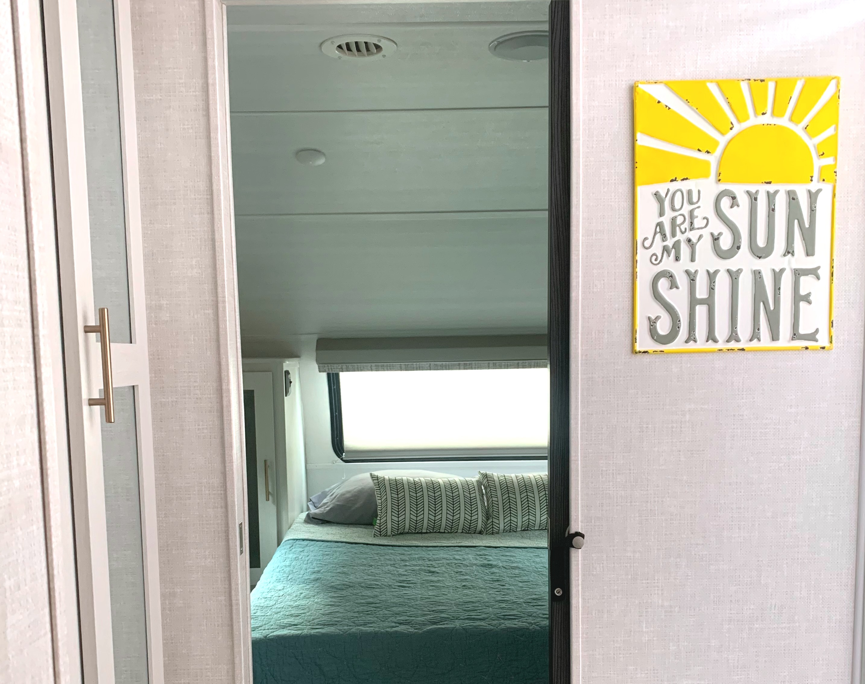 Cozy RV rental bedroom view through an open door, featuring a teal bed and a "You Are My Sunshine" wall sign.. Forest River R-Pod 202 2021