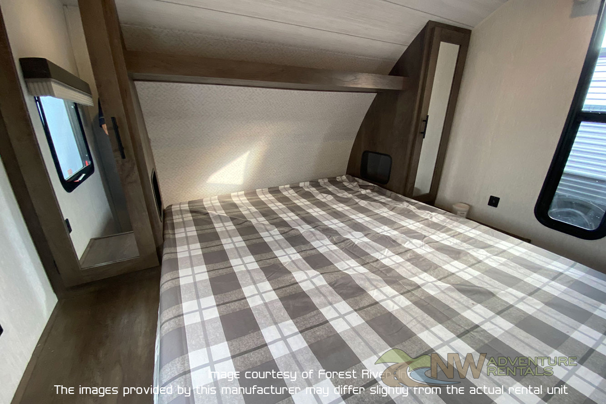 Cozy RV rental bedroom with a plaid bed, side window, and built-in storage, offering comfort for your travels.. Forest River X-Lite 2021