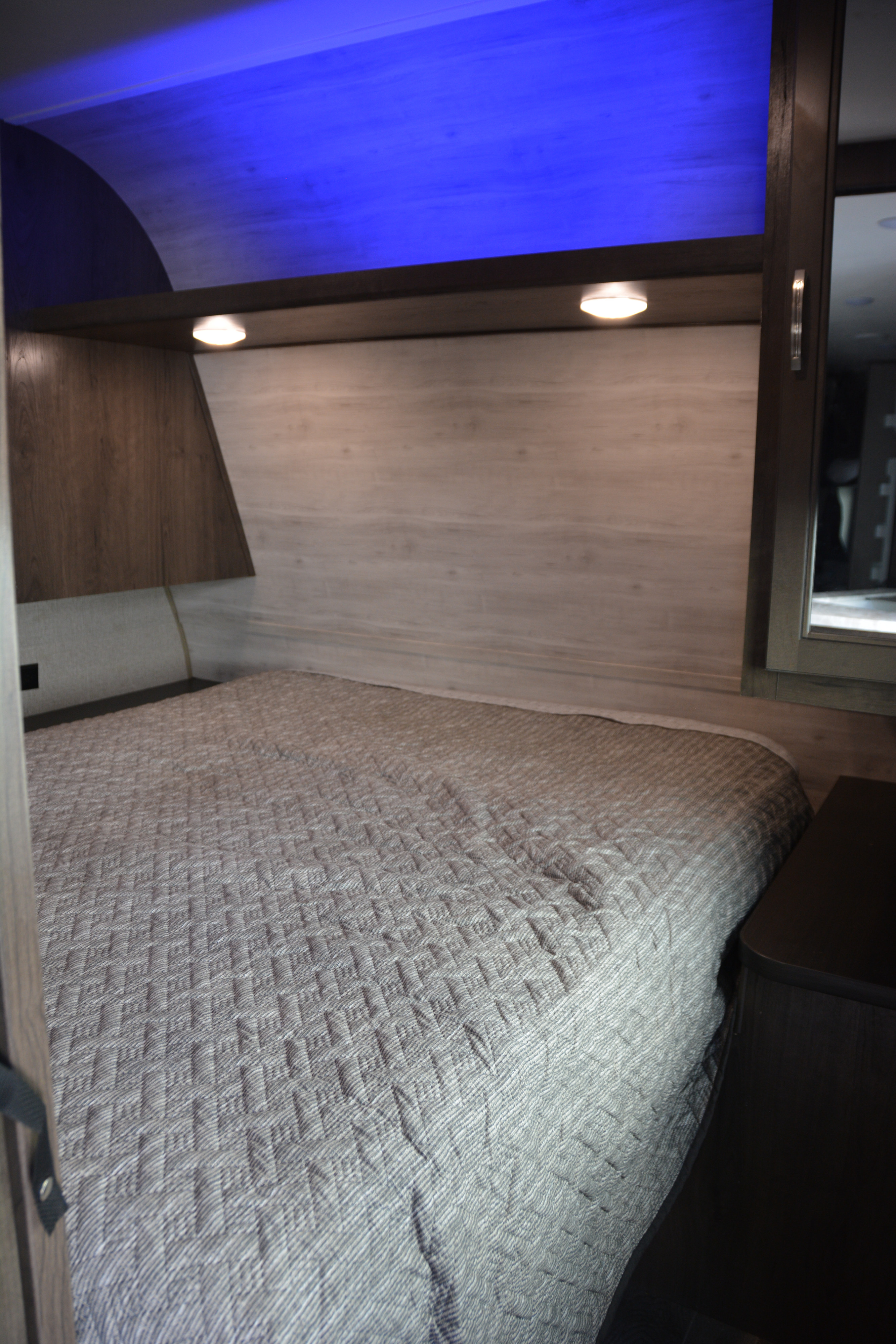 Inside a modern rv rental bedroom, featuring a grey quilted bed, stylish wooden accents, and calming blue LED ceiling lights.. Jayco Jay Flight 2021