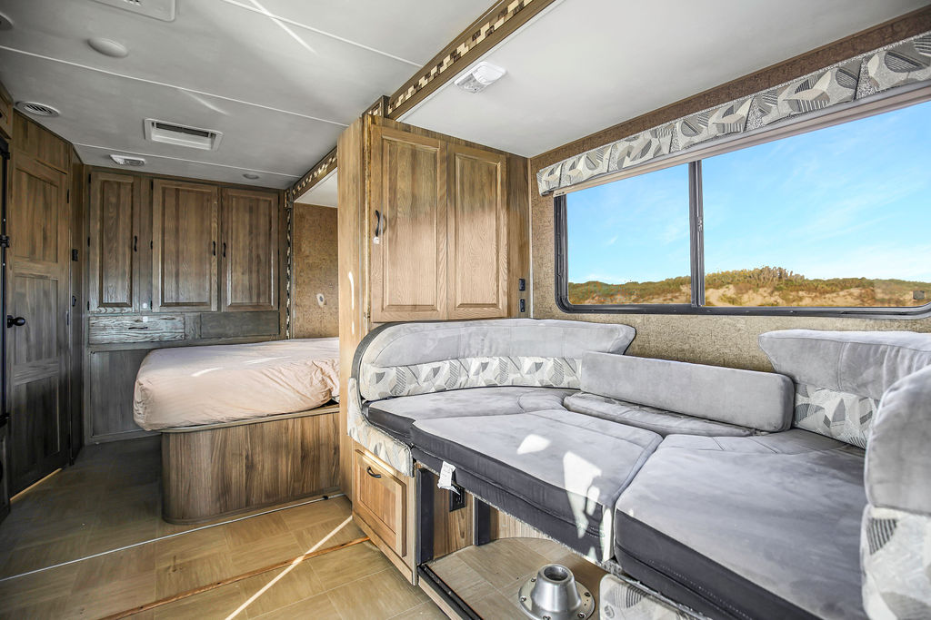 Explore this clean RV rental interior featuring a cozy bedroom, dinette, wood cabinetry, and scenic window views.. Mercedes-Benz Prism 2017