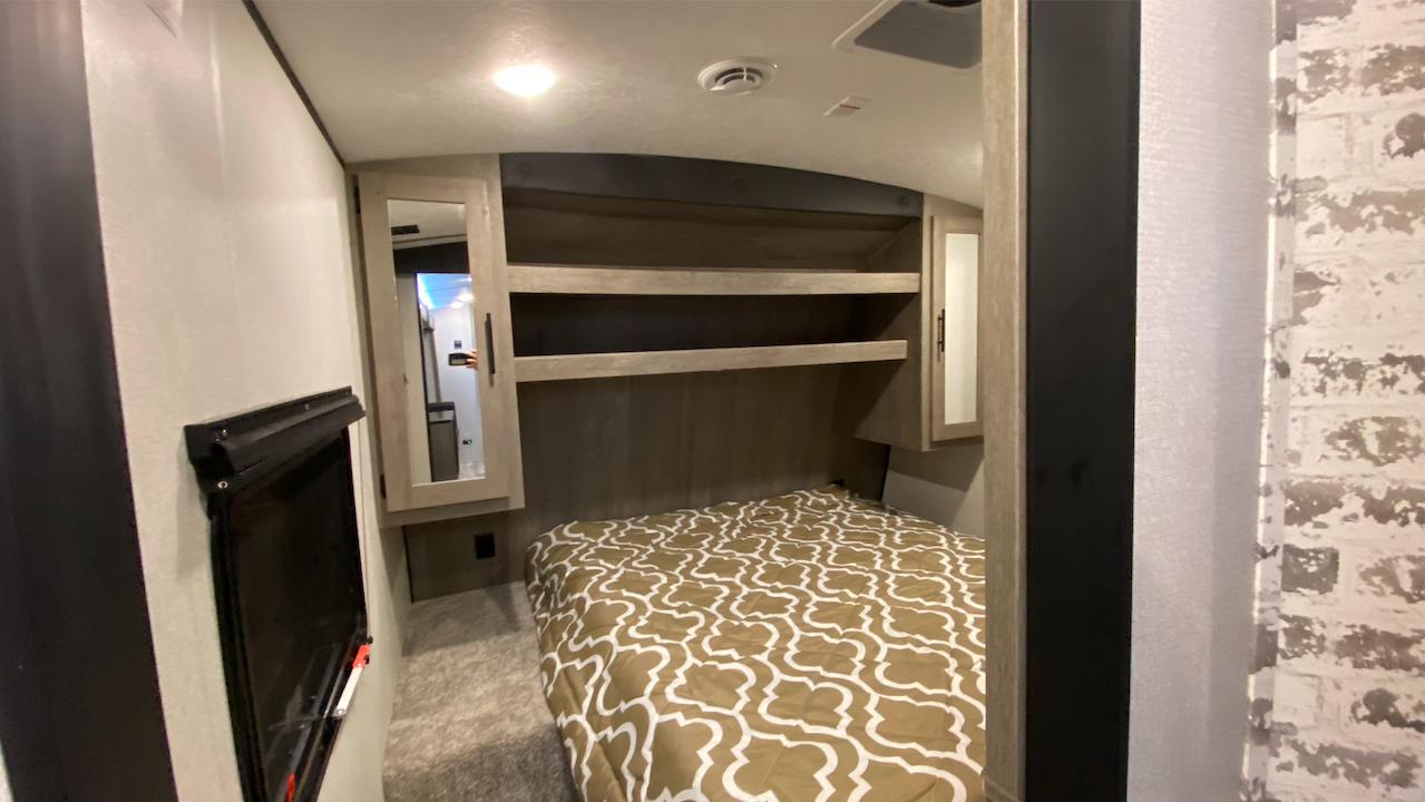 This modern RV rental bedroom features a patterned bed, mirrored storage cabinets, and a mounted TV for comfortable travel.. Keystone Springdale 2021