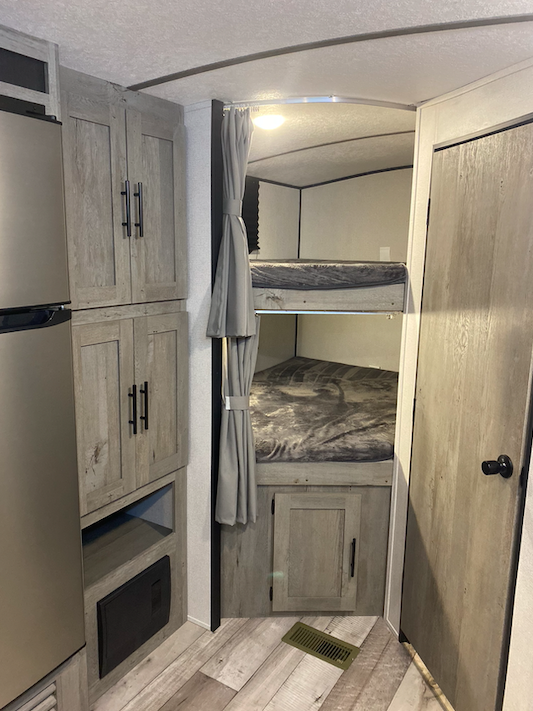 Inside an rv rental: compact living with bunk beds, a refrigerator, and storage cabinets, perfect for family adventures.. Keystone Springdale 2021