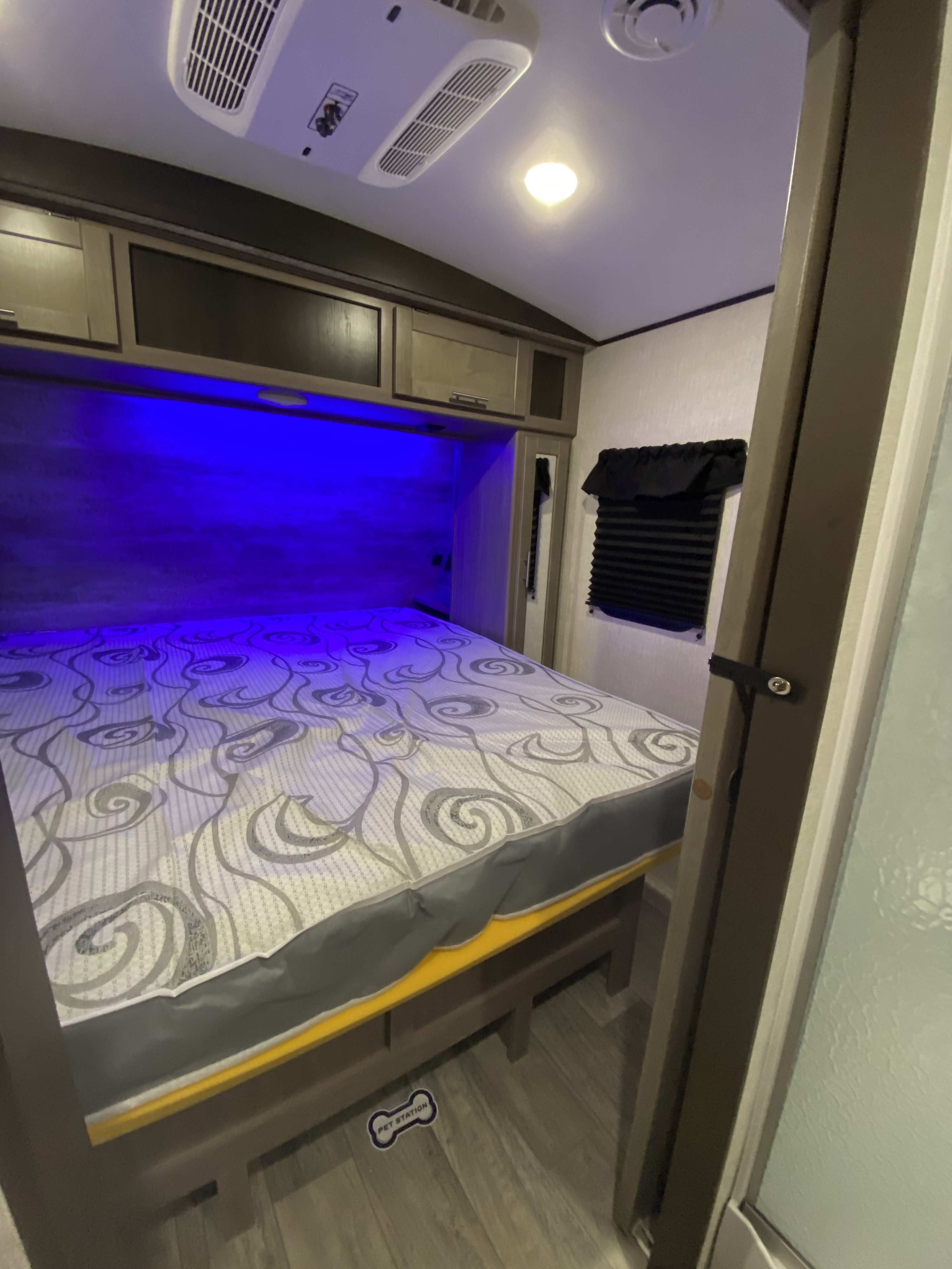 Cozy RV rental bedroom with blue ambient lighting above the bed, overhead AC, and a floor pet station.. Crossroads RV Sunset Trail Super Lite 2021