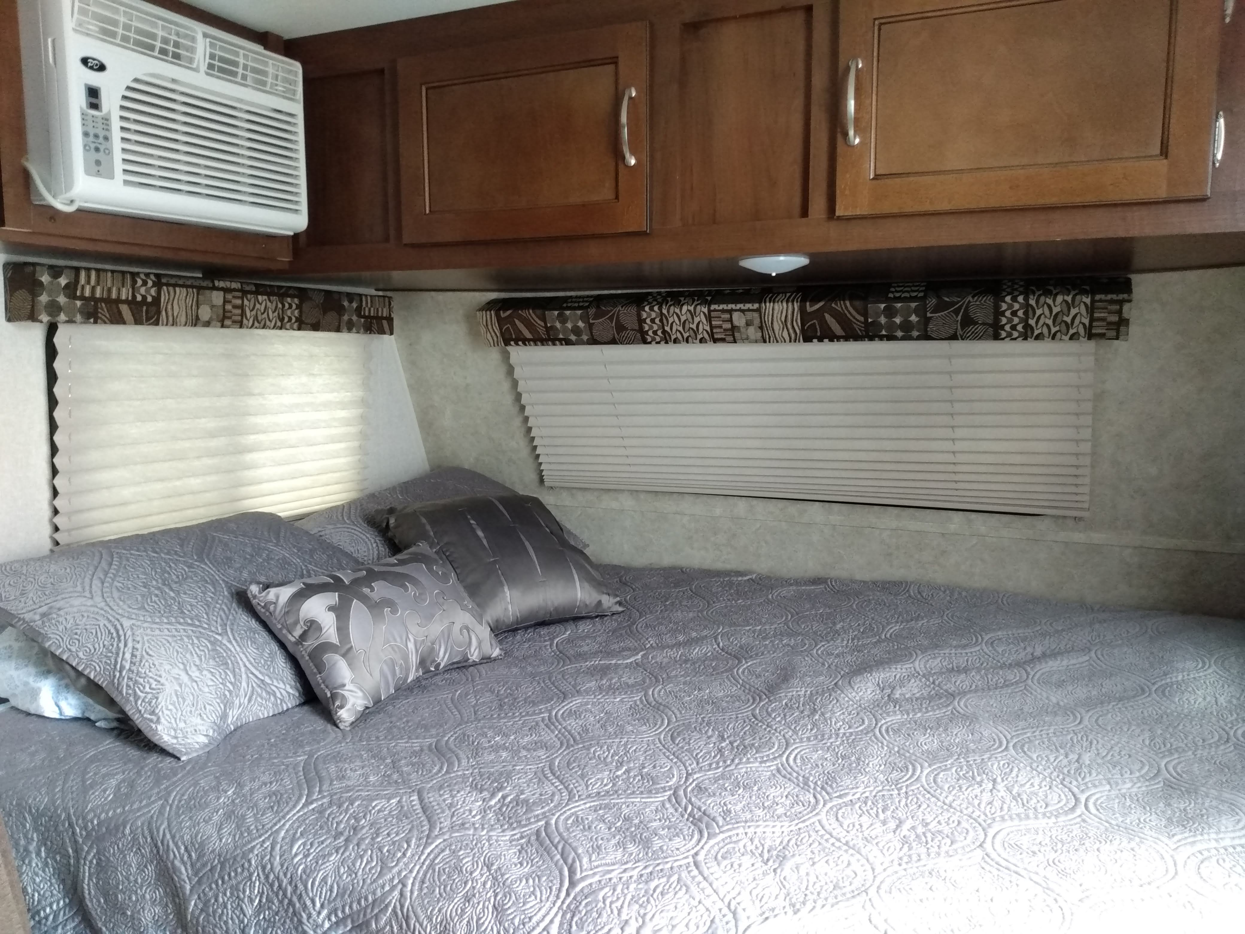 Cozy RV rental bedroom featuring a comfy bed with grey bedding, blinds, overhead cabinets, and an AC unit.. Jayco SLX BAJA 175RD 2017