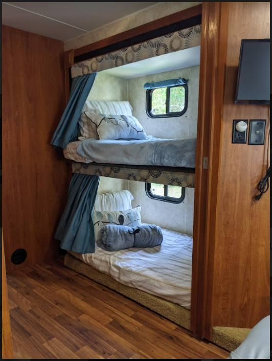 Cozy RV rental bunk beds, perfect for family adventures. Features two beds, windows, and a TV in this comfortable sleeping area.. Forest River Coachmen Freelander 2011
