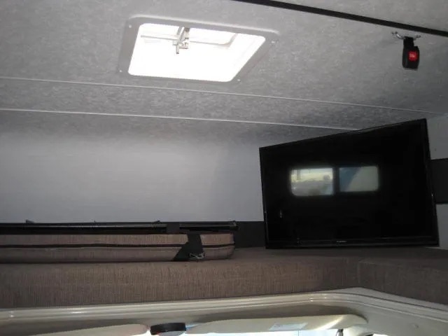 Interior of an RV rental showing the cab-over bunk sleeping area with a TV, safety net, and ceiling skylight.. Coachmen Leprechaun 2021