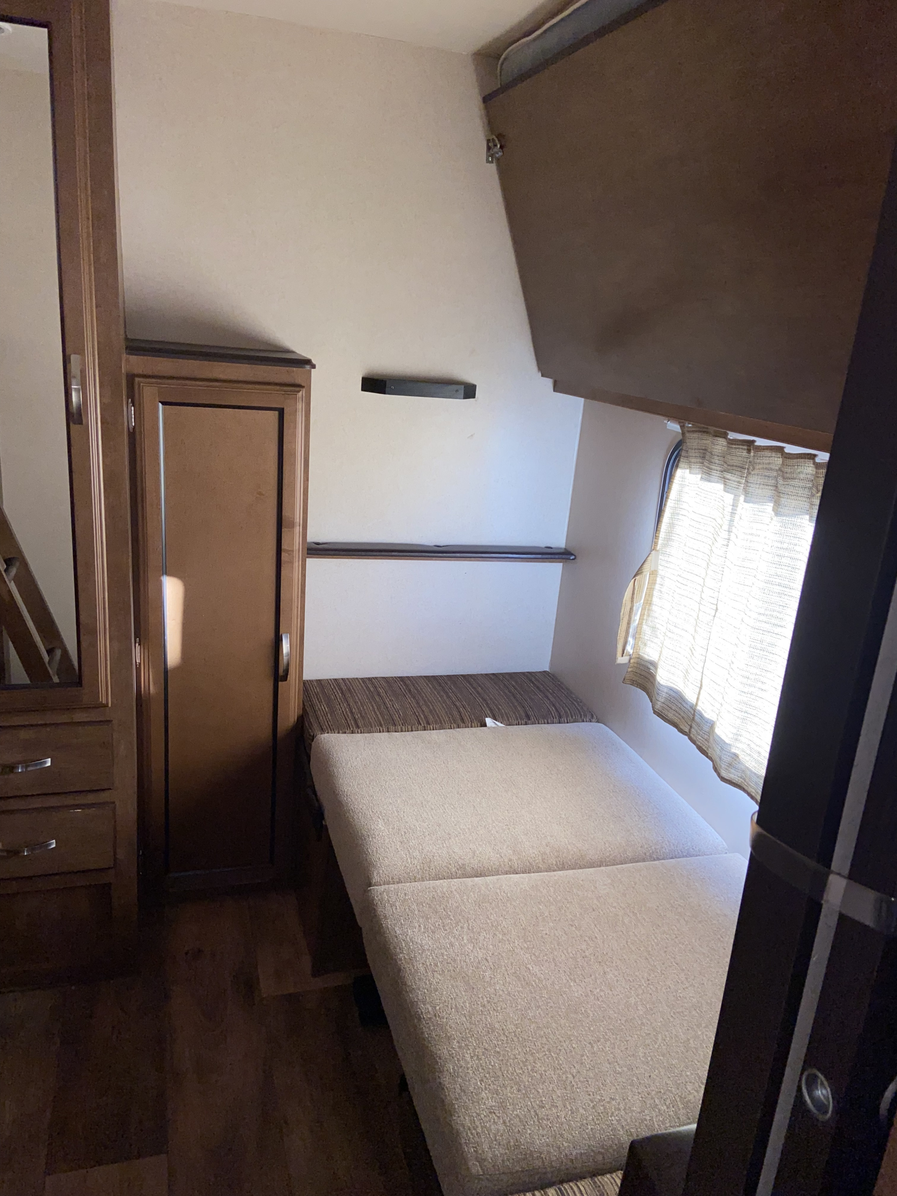 Inside an RV rental: A beige convertible bed/couch, built-in mirror & storage, plus an upper bunk bed, providing compact living space.. Forest River Wildwood 2016
