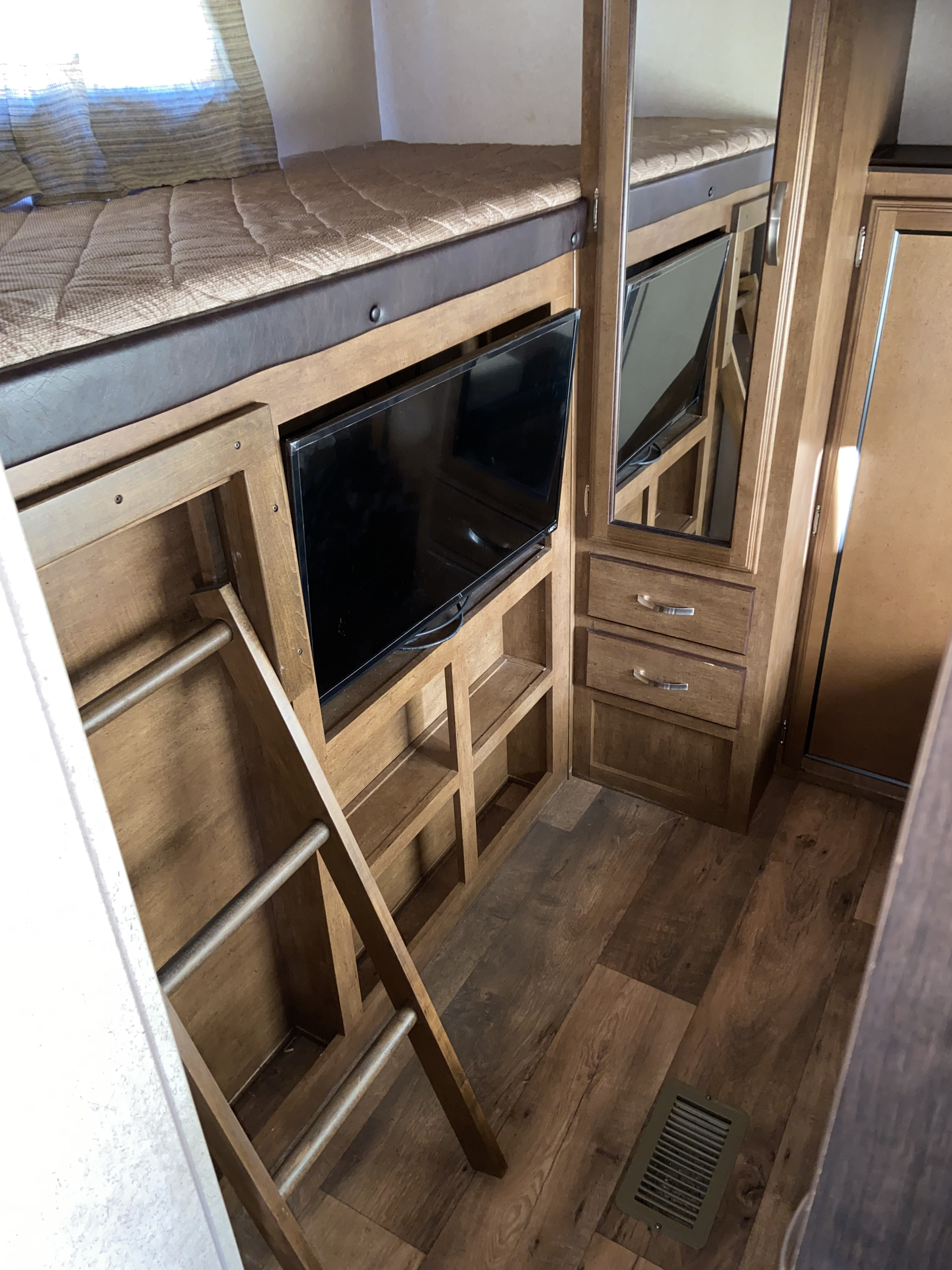 RV rental interior with cozy bunk beds, a ladder, TV, and wood-toned storage cabinets.. Forest River Wildwood 2016