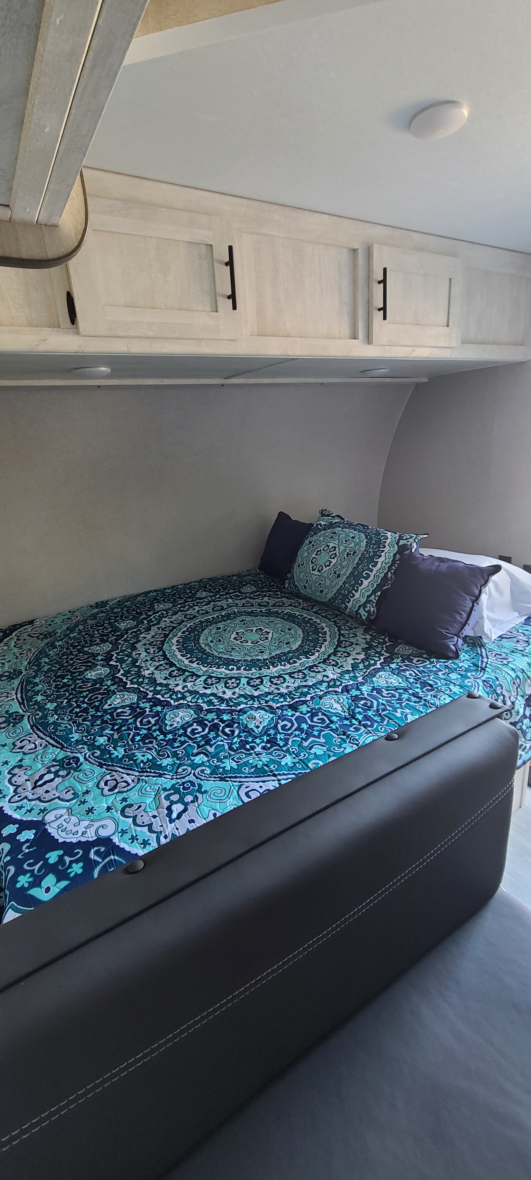 Cozy RV rental bedroom with a blue mandala comforter, overhead cabinets, and black seating.. Shasta BH18 2022