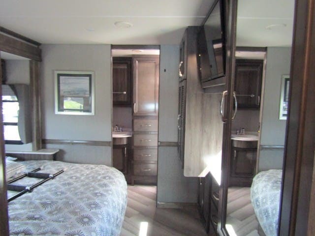 Cozy RV rental interior: Bedroom with patterned bedding & window, plus a compact bathroom vanity & mounted TV. Your travel home.. Fleetwood Bounder 2022
