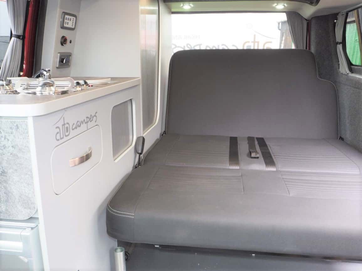 Compact RV rental interior: kitchenette, controls & a comfy bed with seatbelts for comfortable travel.. Ford Transit Custom 2+2 berth Pop Top, Manual 2022