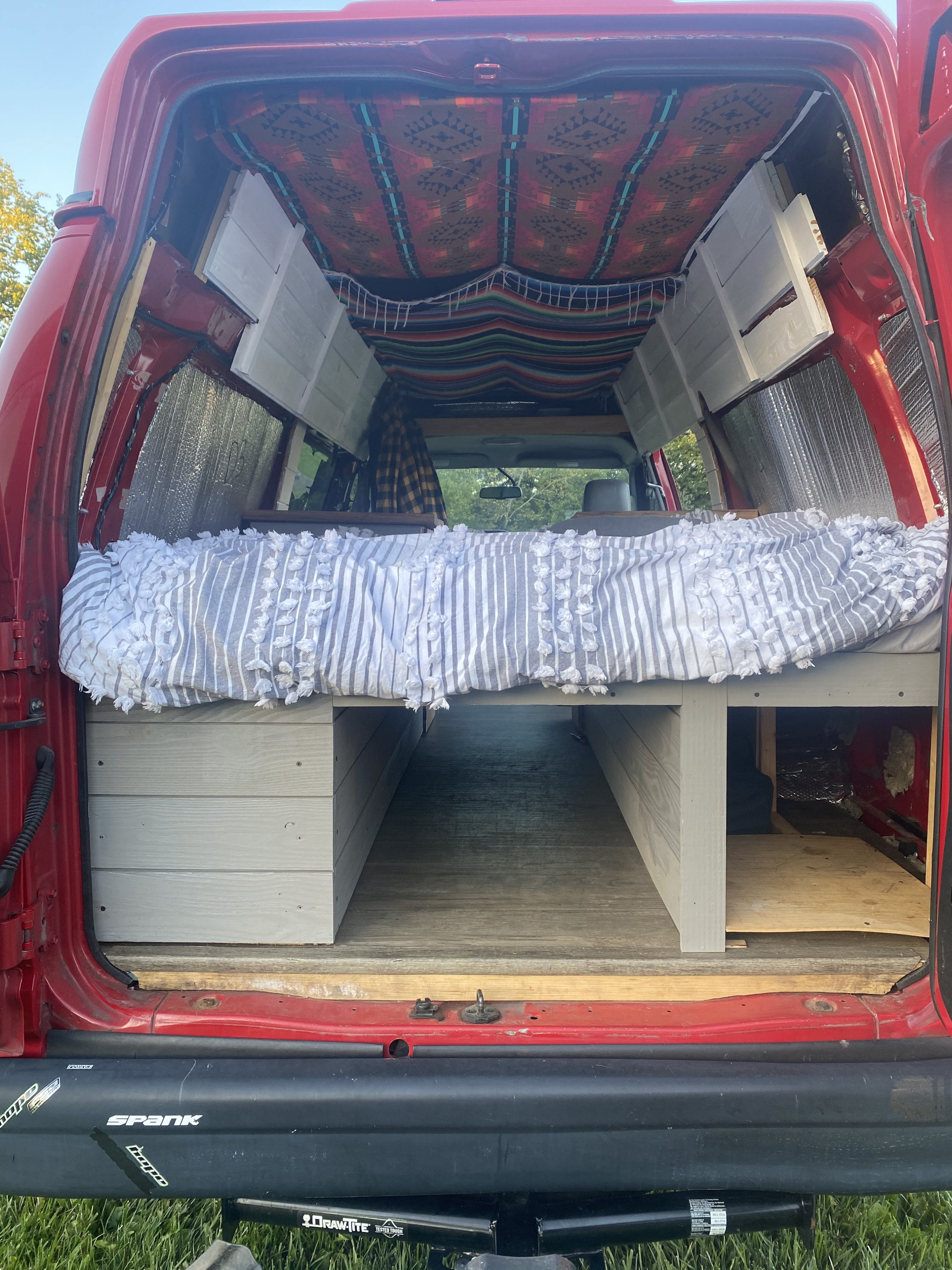 Cozy RV rental: Inside a custom red camper van with comfortable bed, storage, and vibrant decor.. Ford Econoline E250supercab 2011
