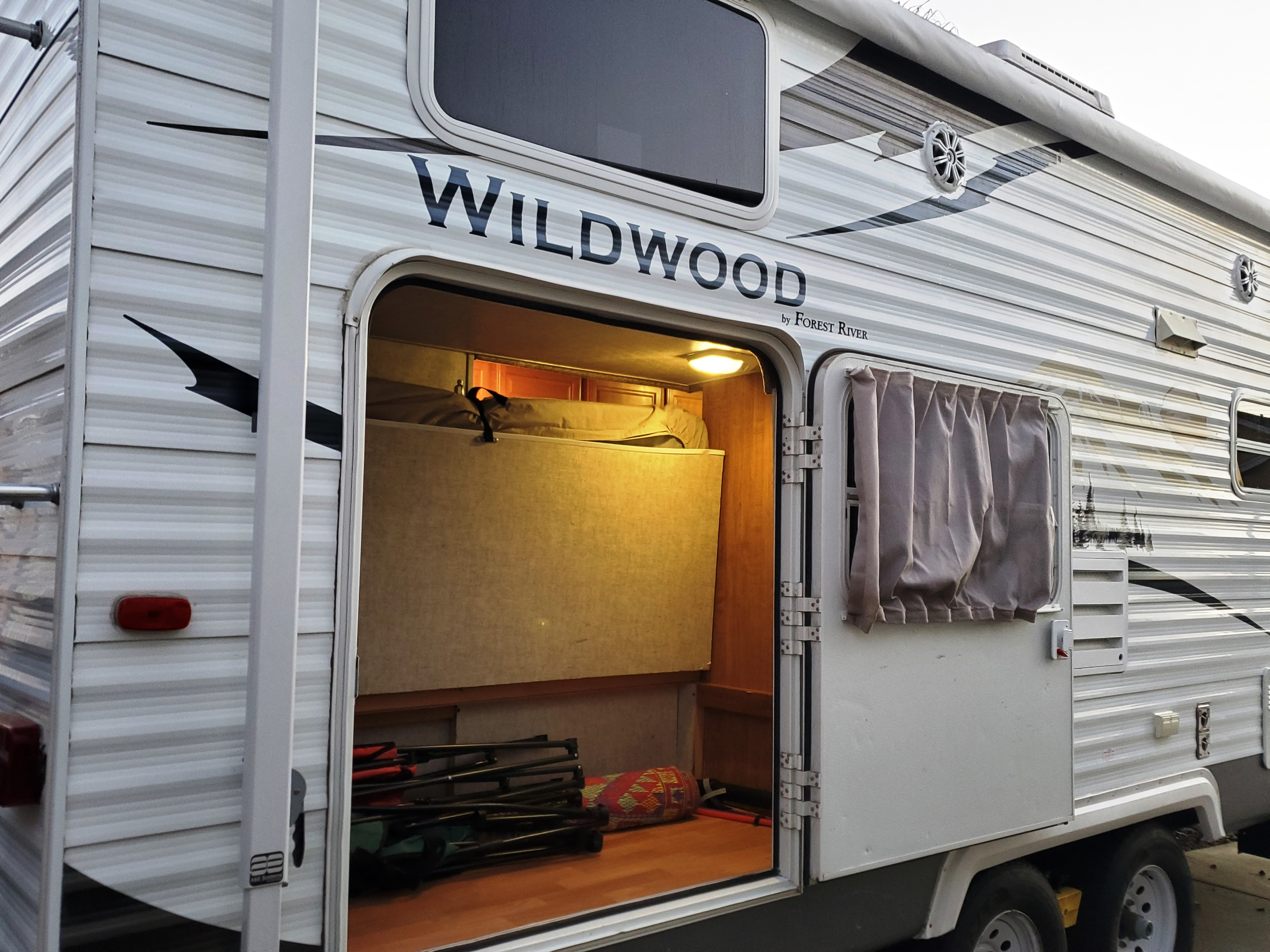 Wildwood travel trailer RV rental with large open storage, revealing folded chairs & a mat, highlighting practical space for travel gear.. Forest River Wildwood 2008
