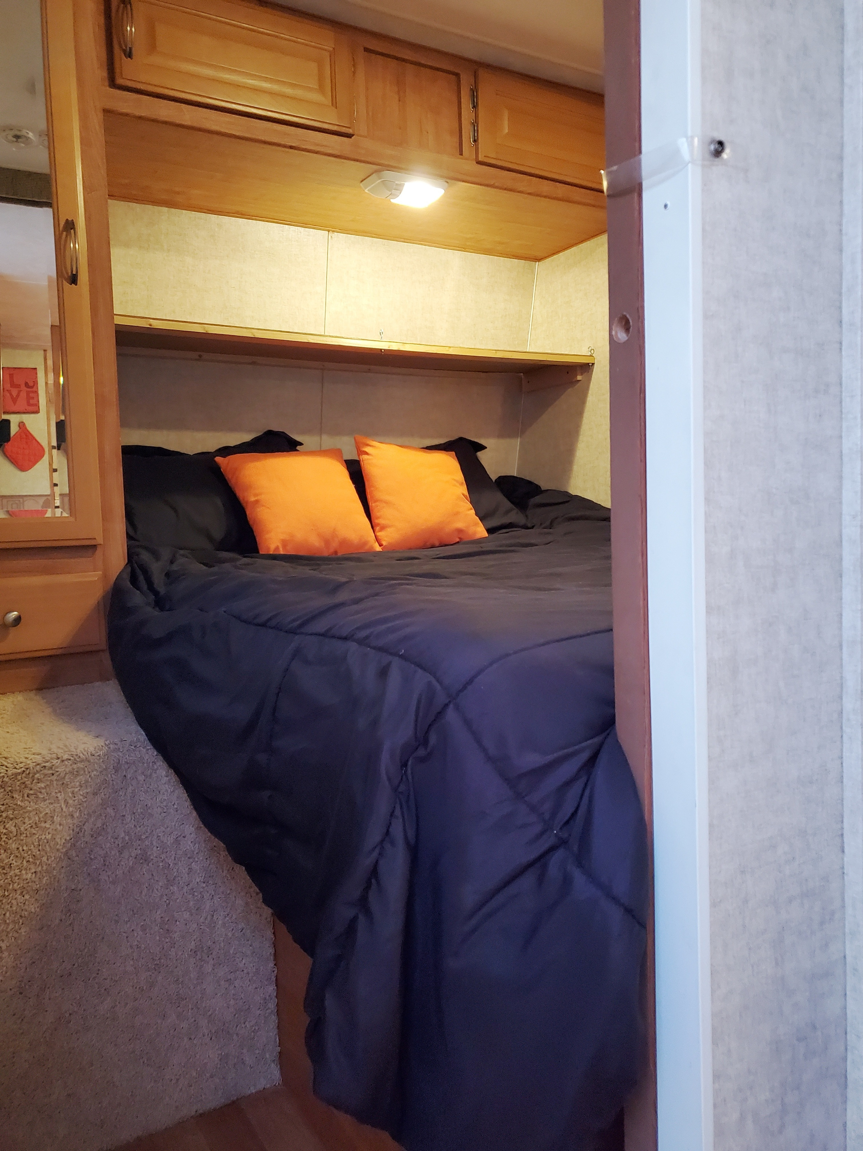 Cozy RV rental bedroom with dark comforter, vibrant orange pillows, and wooden overhead cabinets for storage.. Forest River Wildwood 2008