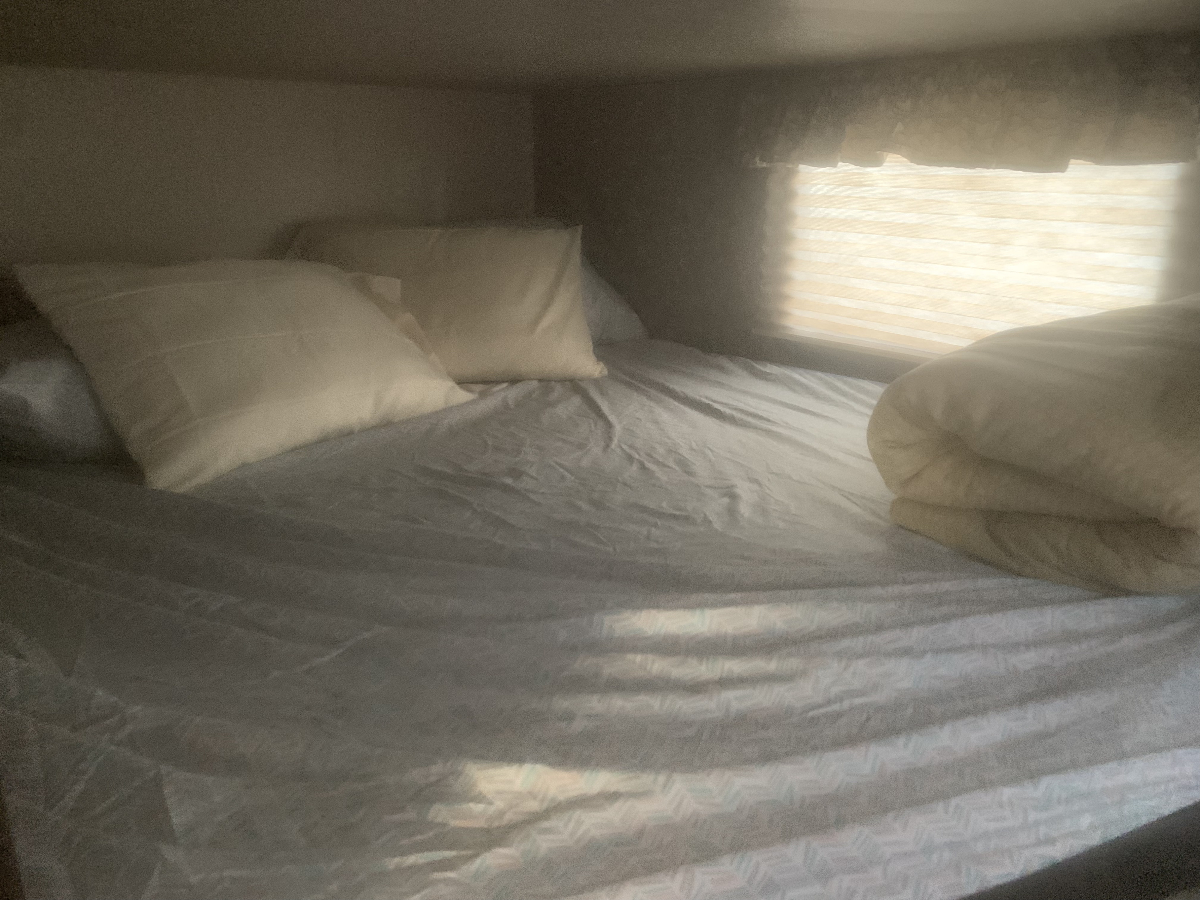 Inside an RV rental: a compact, comfortable bed with pillows and a blanket, brightly lit by a window with blinds.. Keystone Cougar 2017