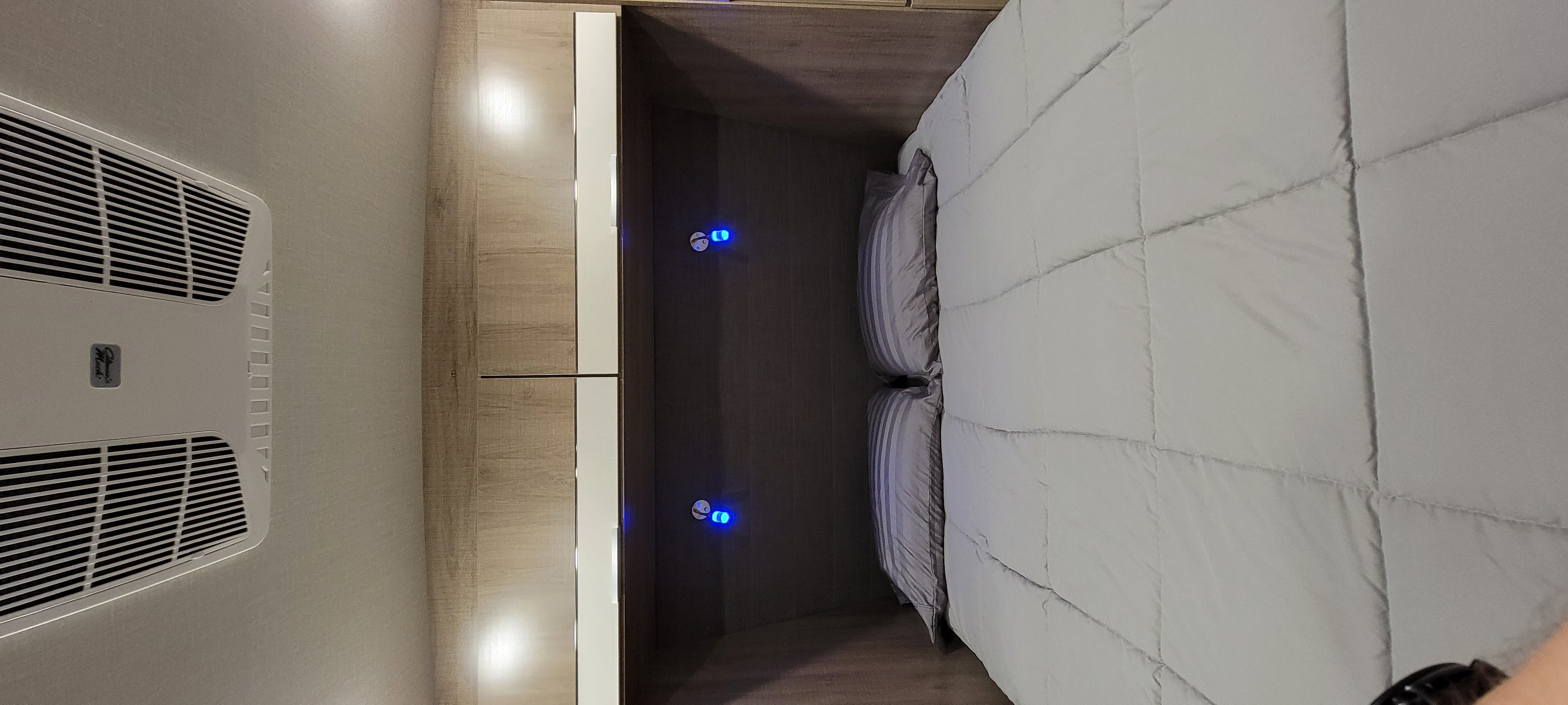Cozy RV rental bedroom with a neatly made bed, overhead AC unit, and illuminated storage beside the bed.. Grand Design 2800BH 2021