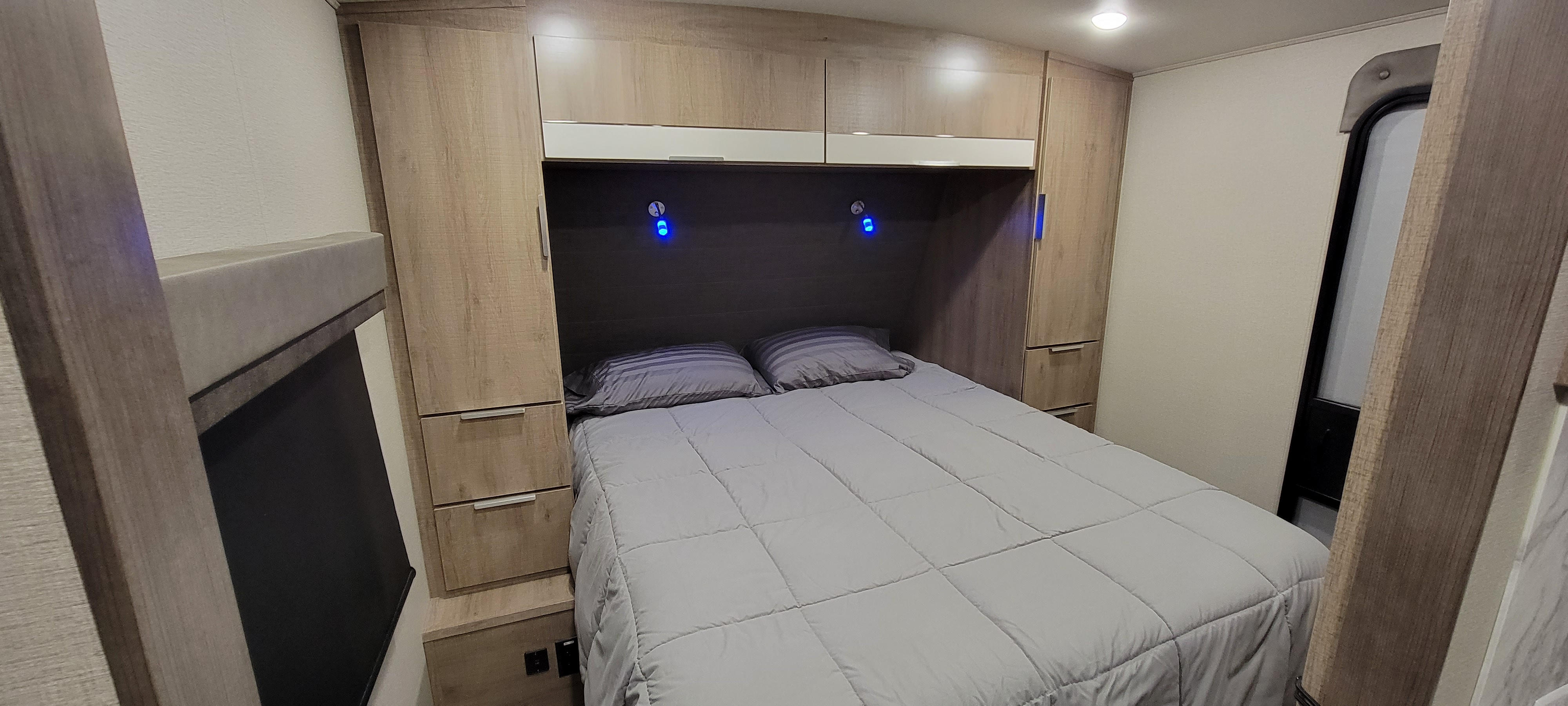 Cozy RV rental bedroom with a grey bed, overhead cabinets, and side wardrobes providing ample storage in a compact space.. Grand Design 2800BH 2021
