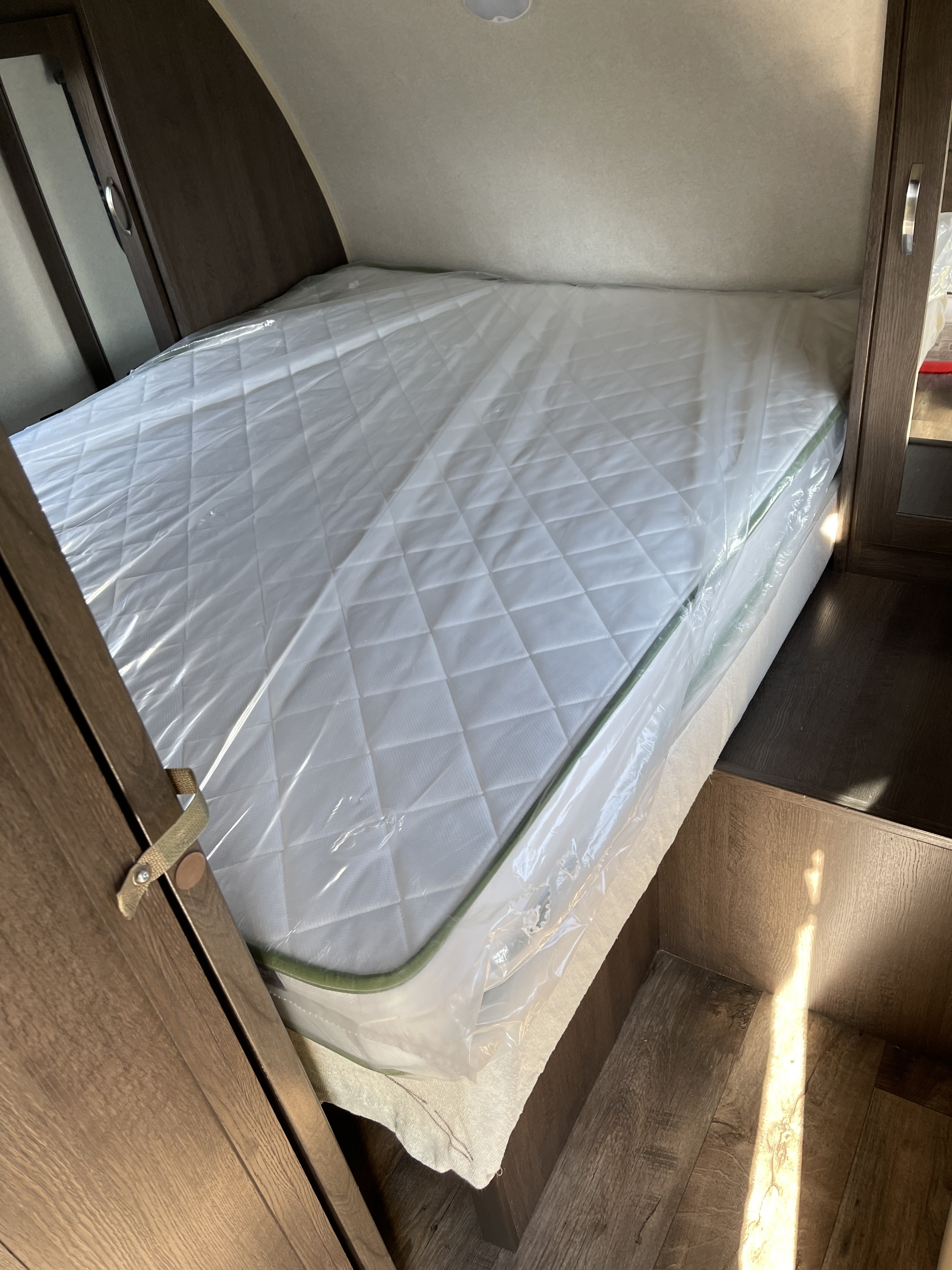 RV rental bedroom features a new, plastic-covered mattress & wood accents.. Forest River Cruise Lite 2019