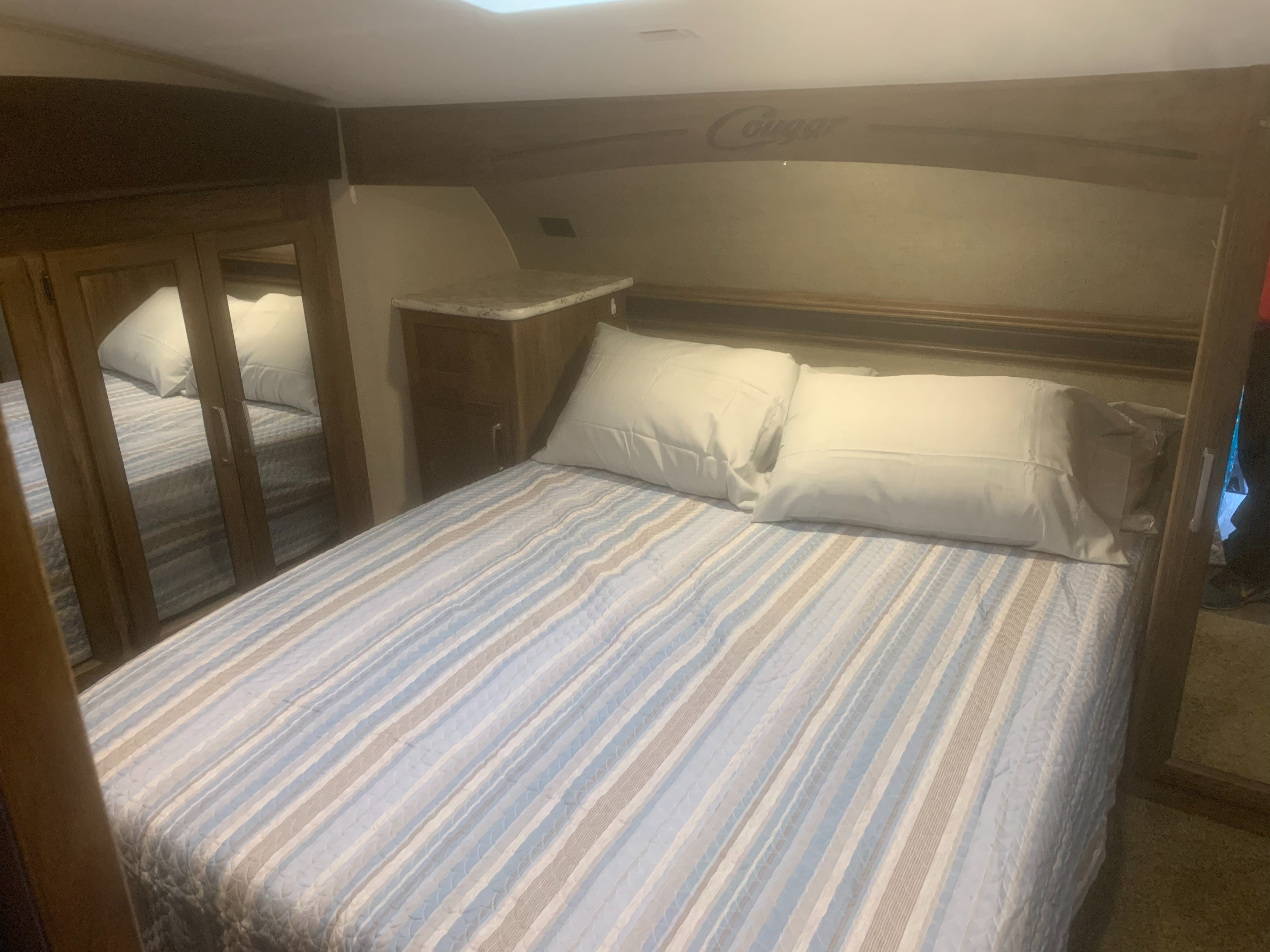 Cozy RV rental bedroom featuring a comfortable bed with striped linens, mirrored wardrobe, and overhead storage.. Keystone Cougar 2017