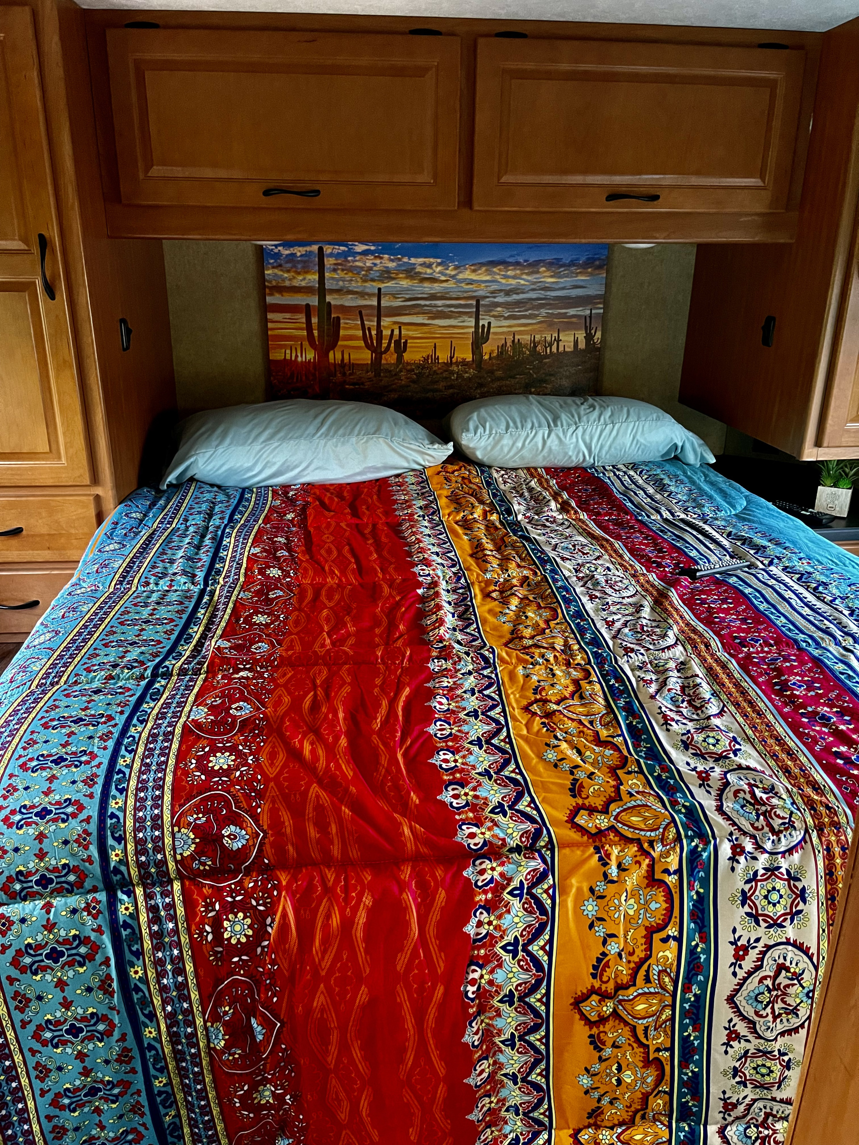 RV rental bedroom featuring a vibrant patterned comforter, saguaro cactus mural, and wood cabinetry.. Other Four Winds Majestic 2017