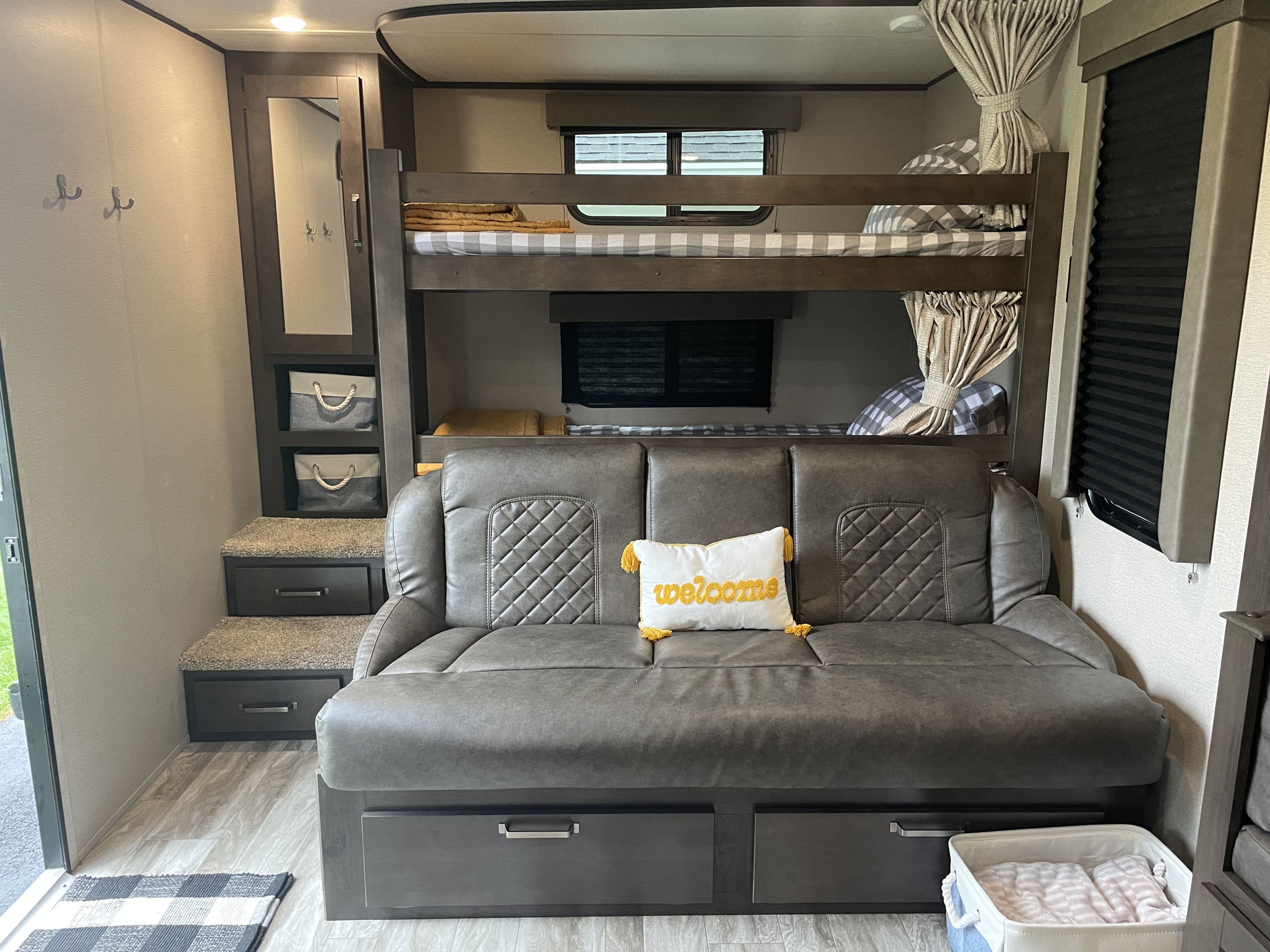 Inside a comfortable RV rental: bunk beds with privacy curtains, a gray sofa bed, built-in storage, and mirror.. Grand Design Transcend 265bh 2021