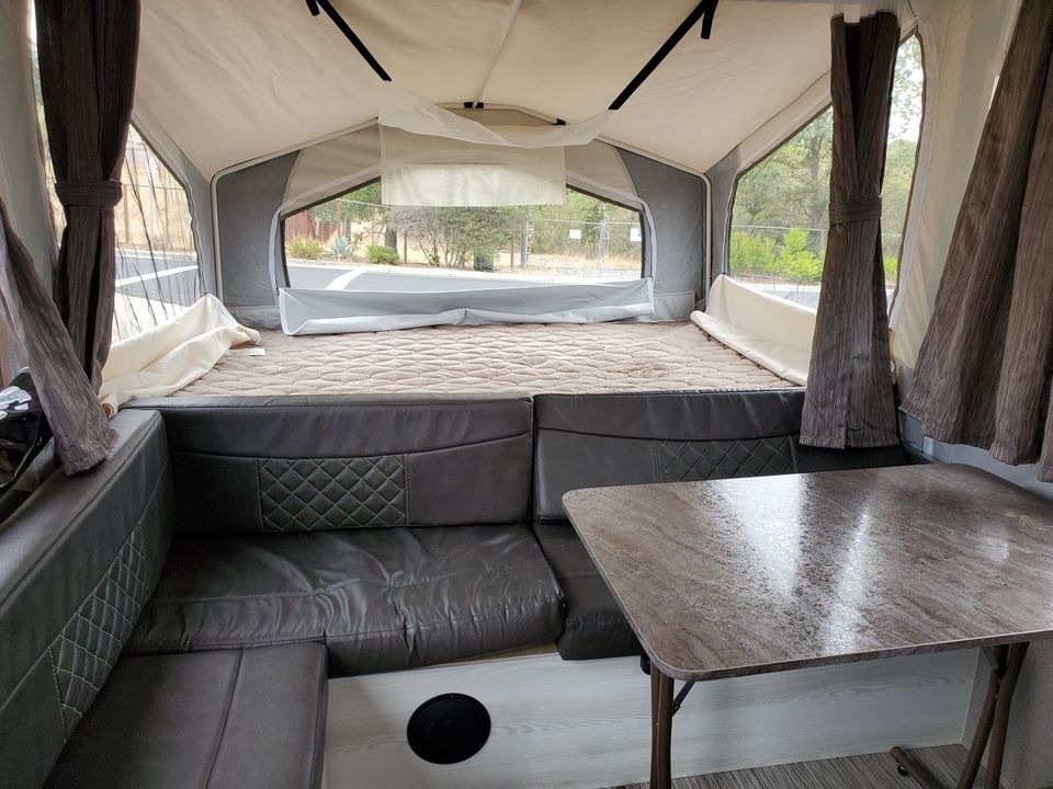Explore this cozy pop-up rv rental interior, featuring a comfortable bed, L-shaped dinette, and dining table.. Forest River Rockwood ESP 2019