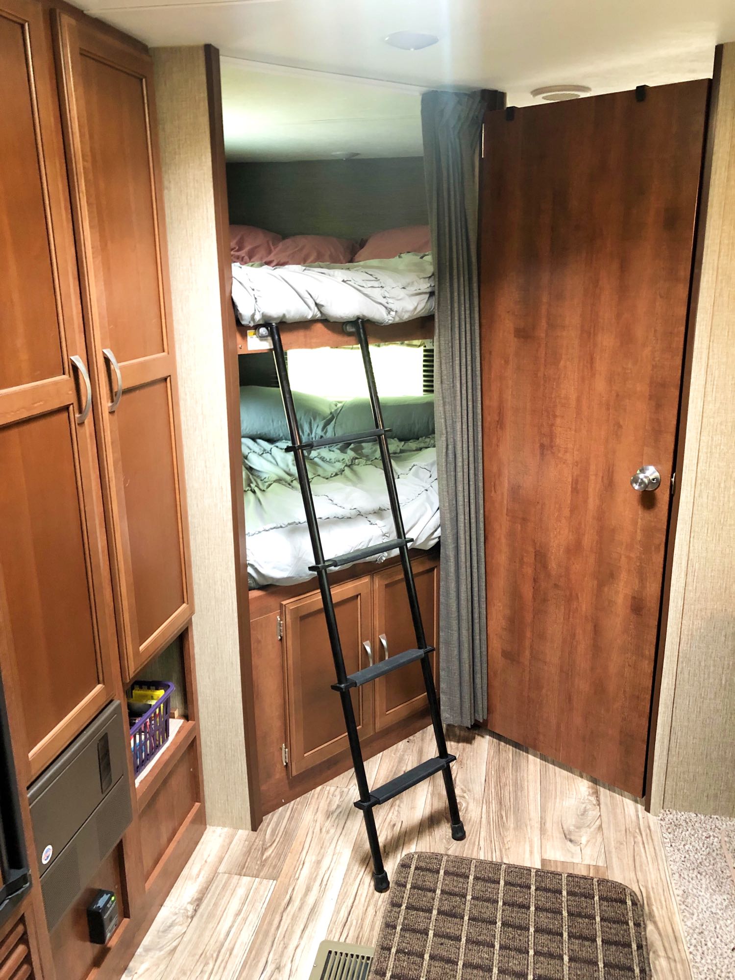 RV rental bunk beds with a black ladder, soft bedding, wooden cabinets, and a door on wood-look flooring.. Keystone Passport 2017