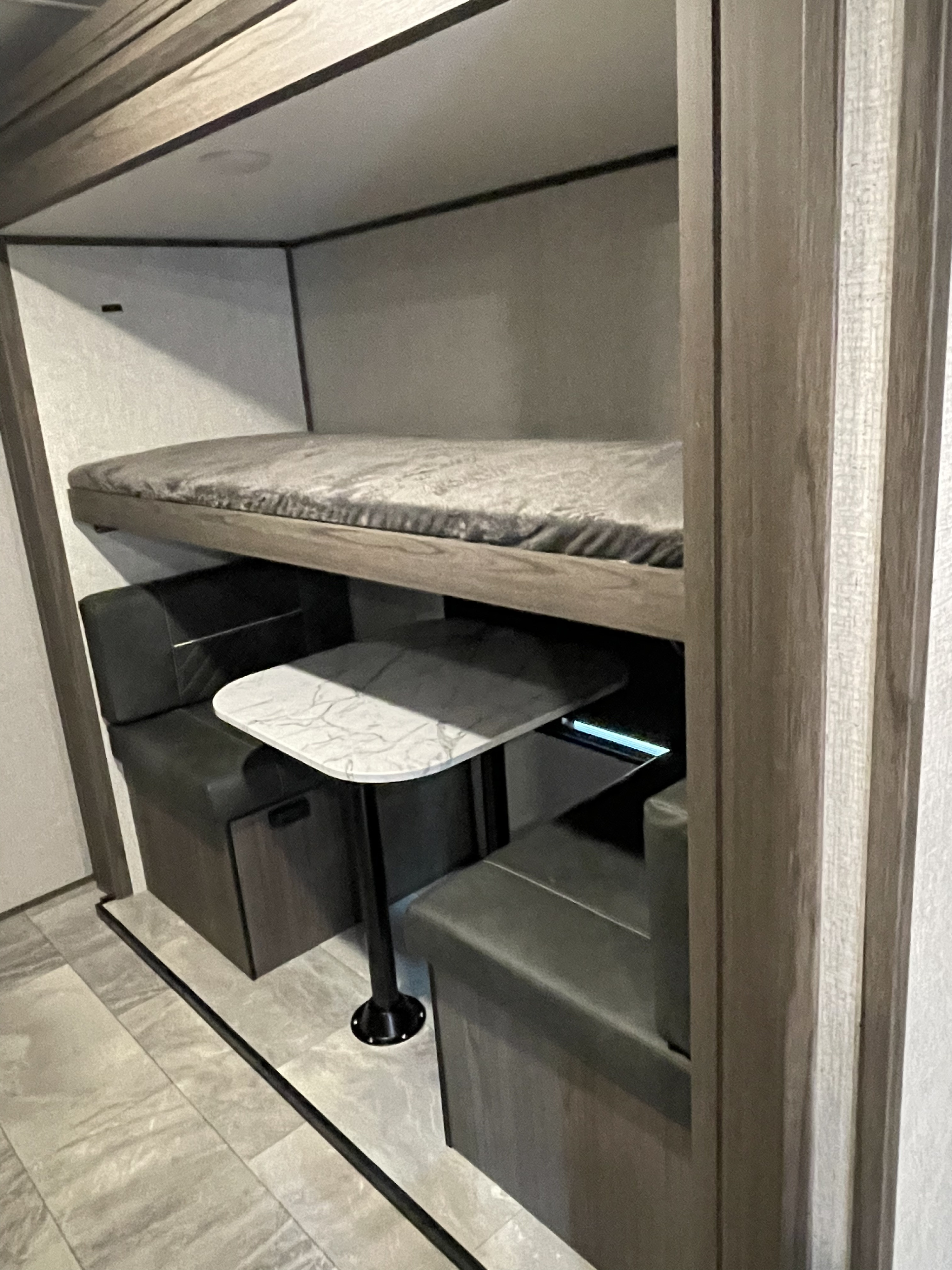 This RV rental interior features a cozy bunk bed situated over a dinette with dark bench seating and a white marbled table.. Dutchmen Other 2021