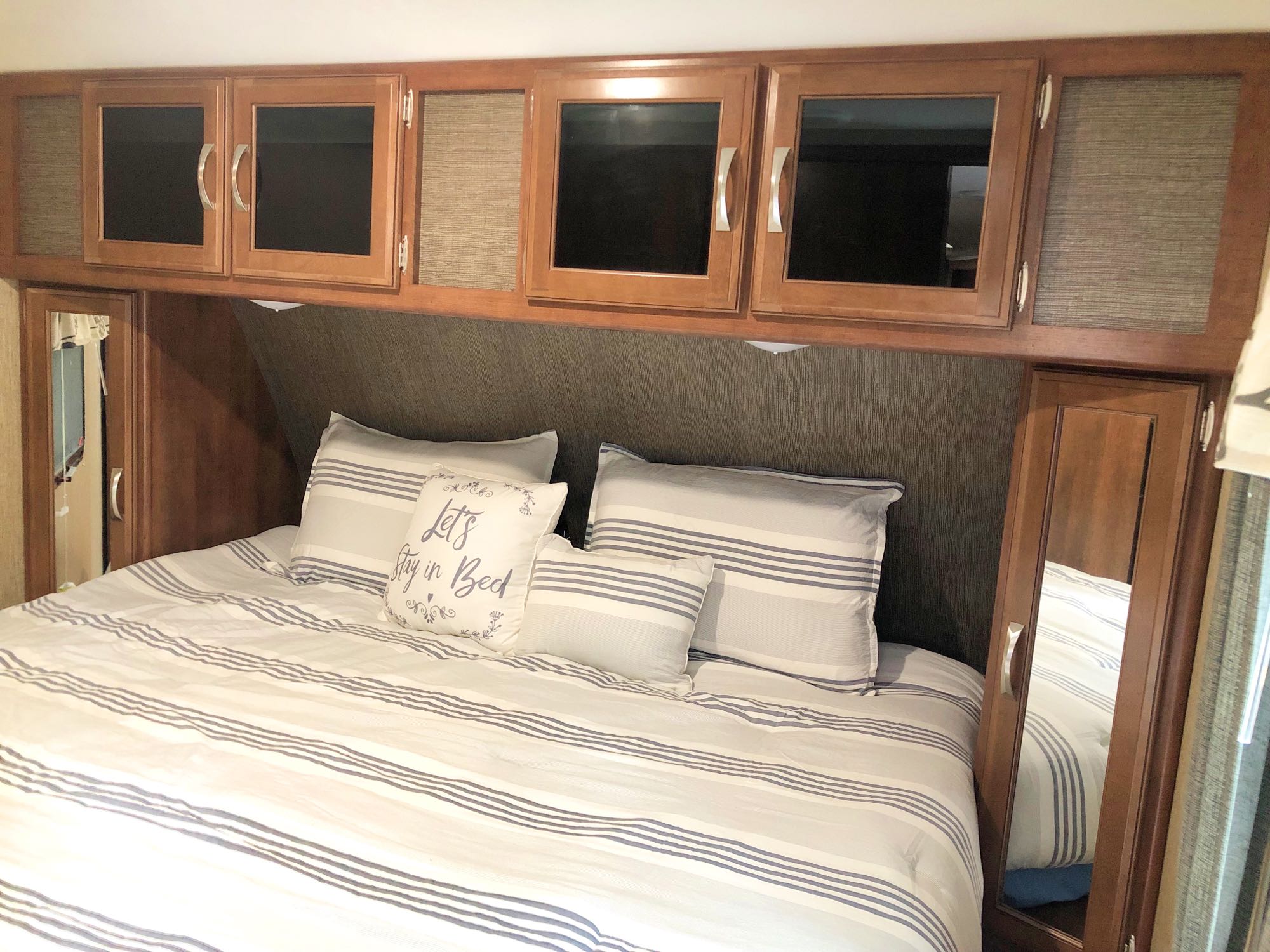 Relax in this comfy RV rental bed! Striped bedding, ample overhead cabinets & mirrors enhance this cozy space.. Keystone Passport 2017