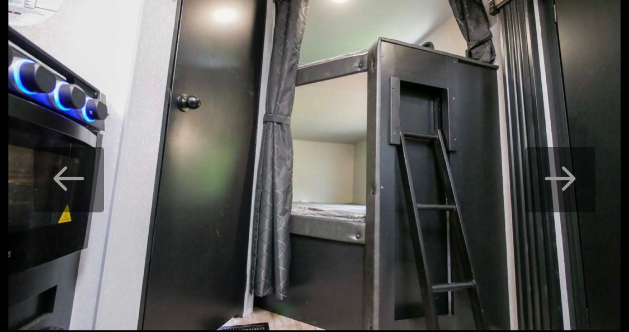 RV rental interior featuring a compact kitchen (left) with illuminated knobs, plus bunk beds with ladder & curtain.. Forest River Cherokee Grey Wolf 2021