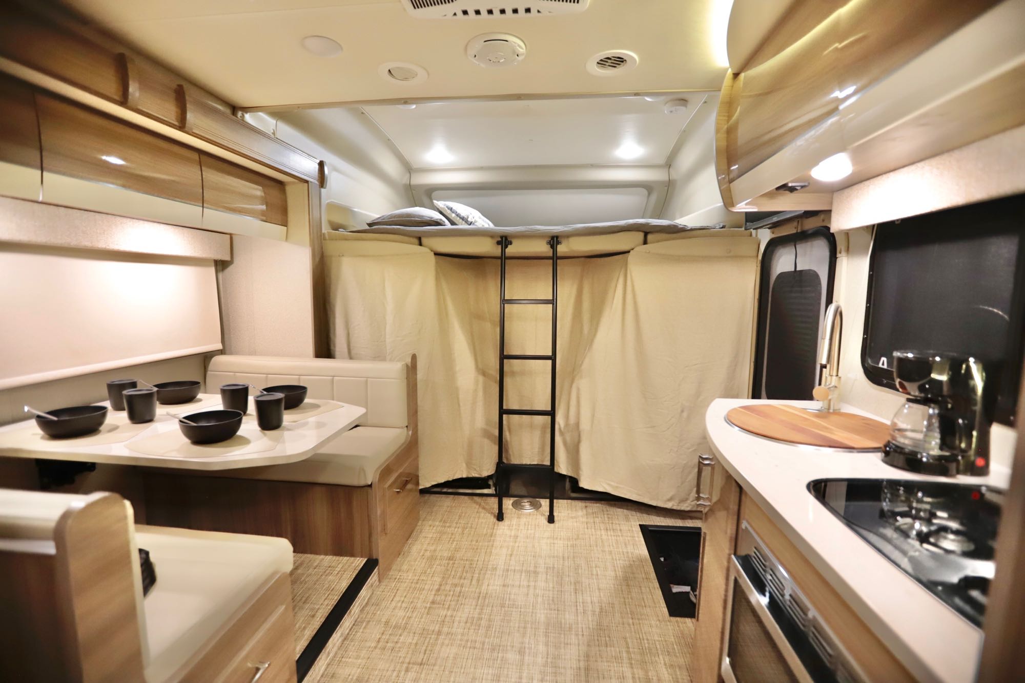 This RV rental interior features a cozy bunk bed, dining nook, and compact kitchen area.. Jayco Qwest 2019